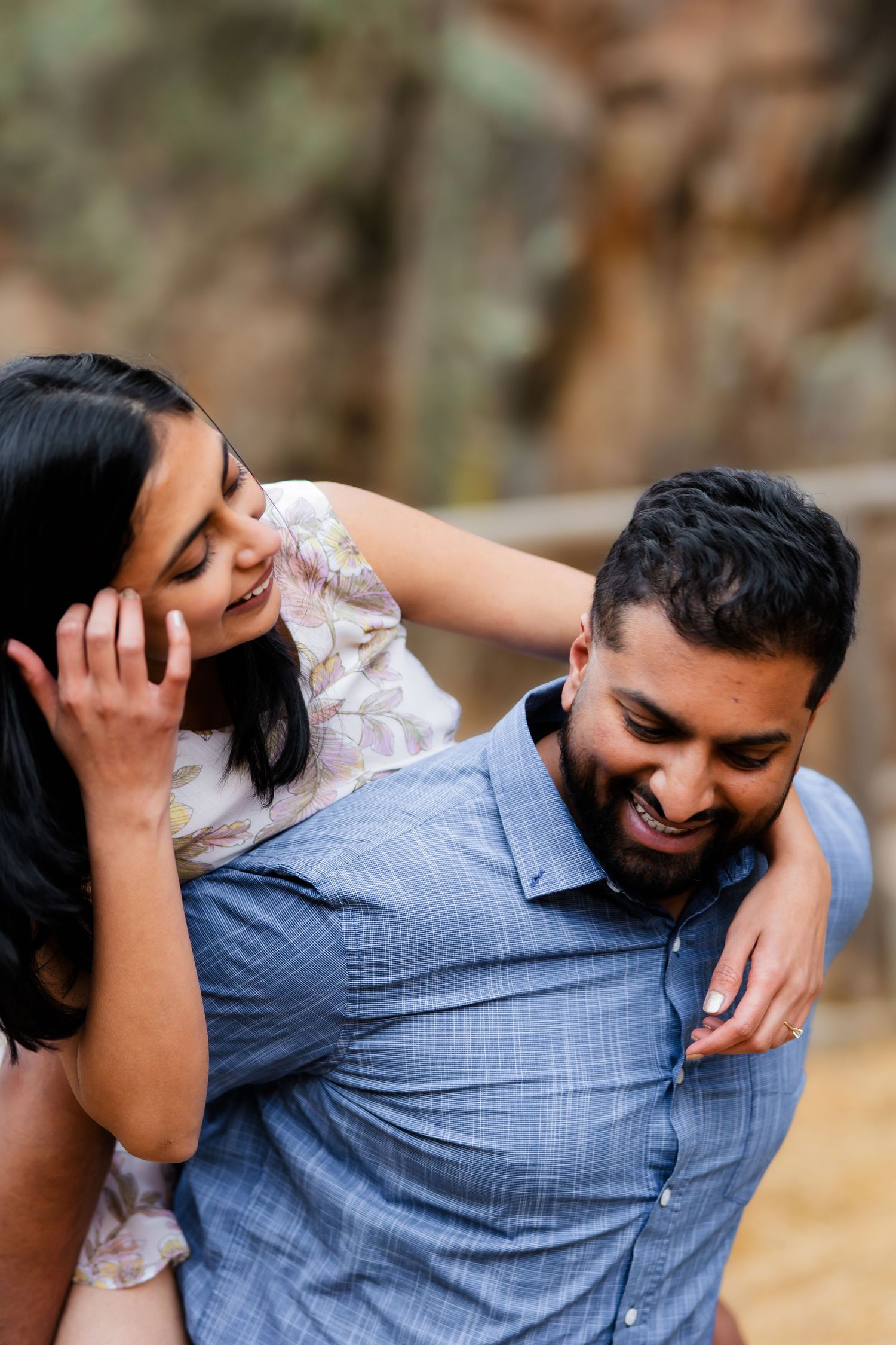A playful couple sharing a candid laughing moment in casual attire outdoors.