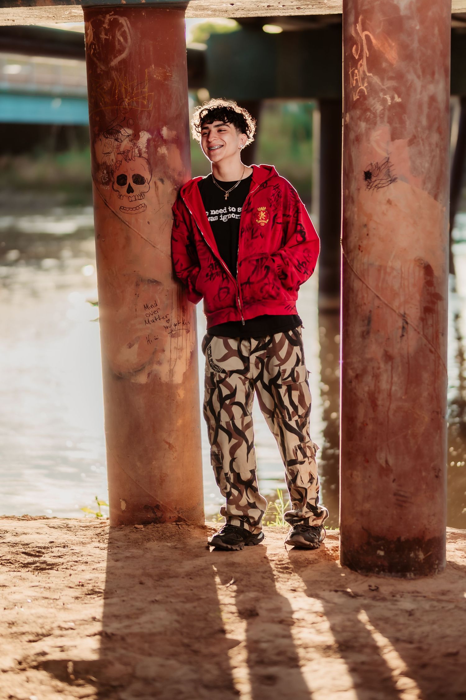 Stylish outfit with red hoodie and patterned pants posed between rustic pillars.