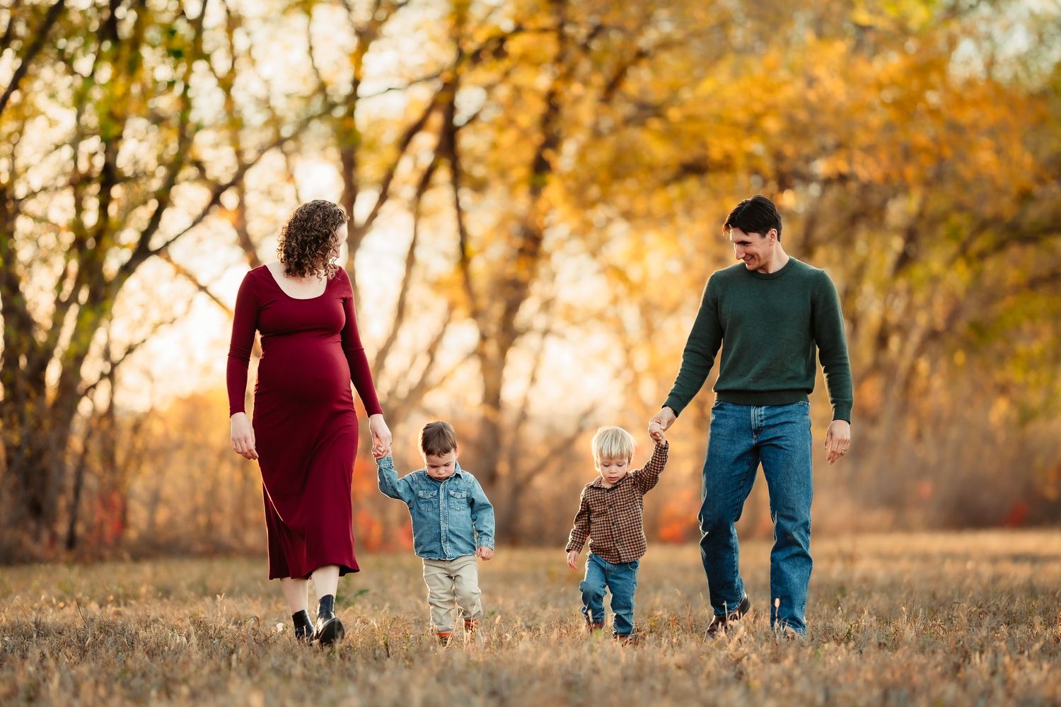 A family walks together through a golden autumn field at sunset holding hands.