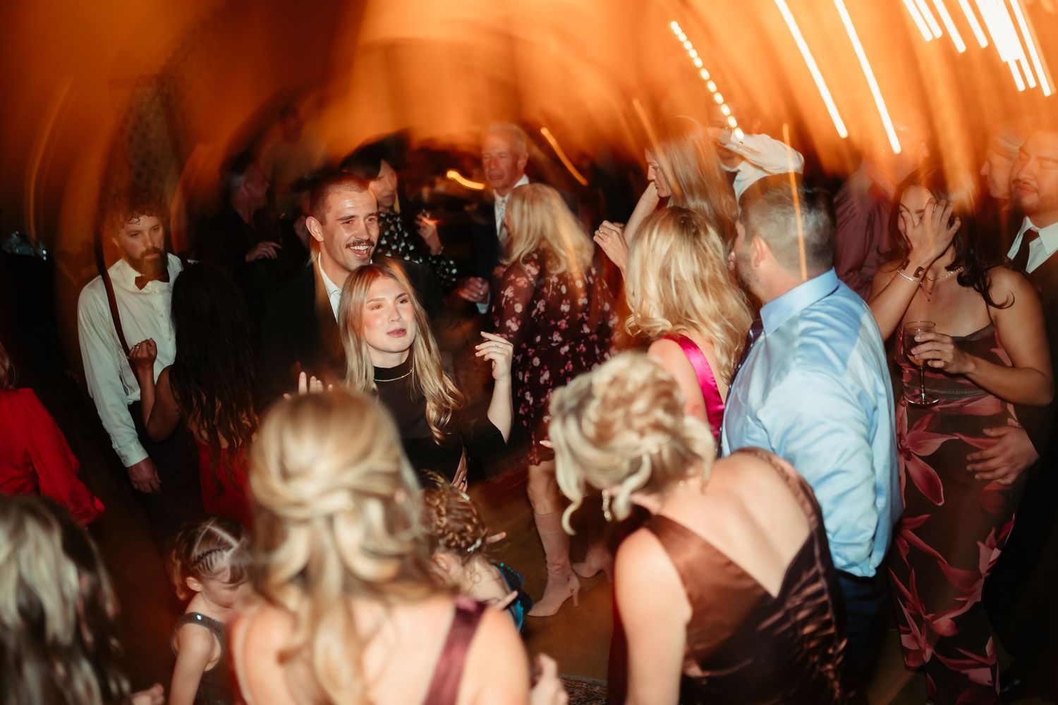 A crowded dance floor filled with people dancing and celebrating at a party with warm lighting and motion blur effects.