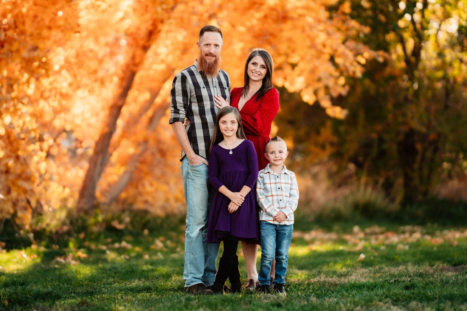 Family poses together against vibrant orange autumn foliage during a fall outdoor photo session.
