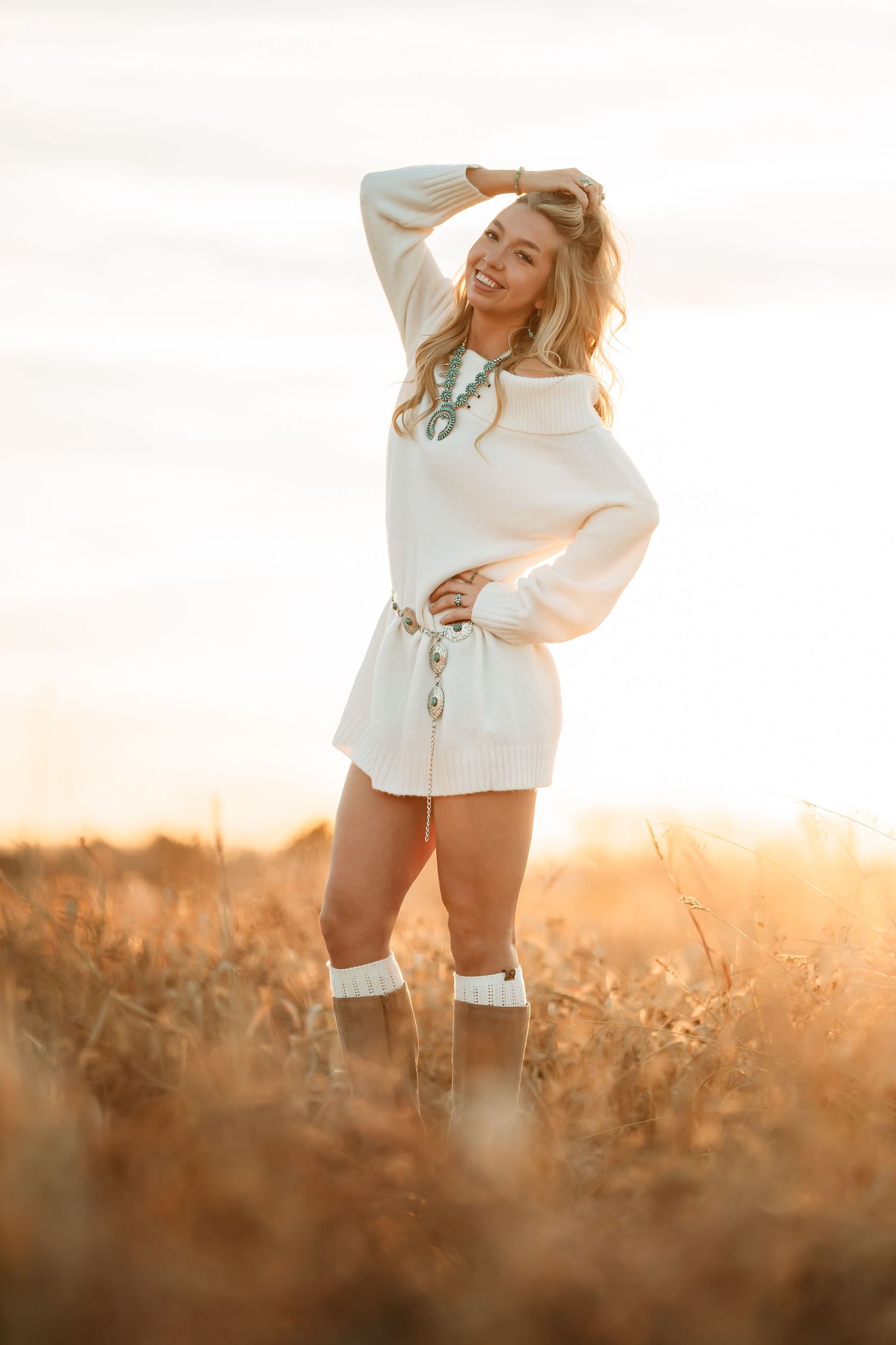 A figure stands in a sunlit field wearing a white sweater and boots during golden hour, creating a dreamy atmosphere.