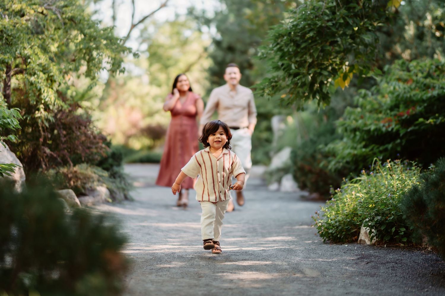 A couple walks together on a tree-lined path in a lush garden setting during a sunny afternoon.