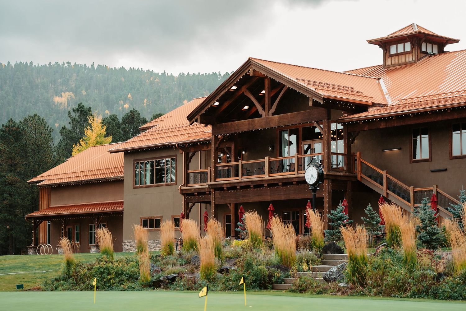 A rustic mountain lodge with timber frame architecture and terracotta roof tiles nestled against a forested hillside.