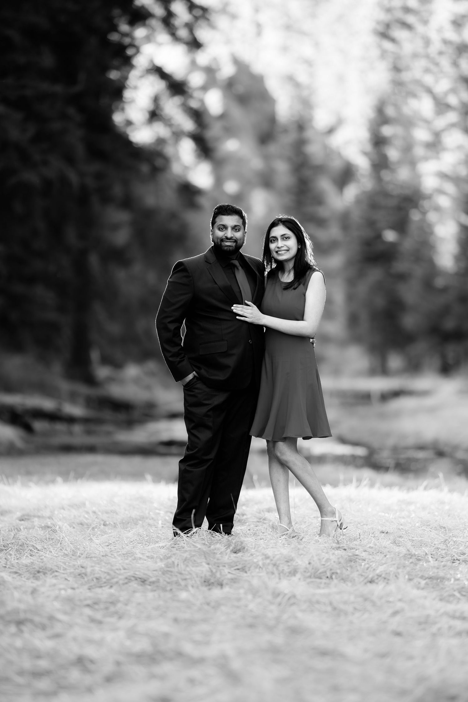 A black and white portrait of a couple in formal wear standing together outdoors.