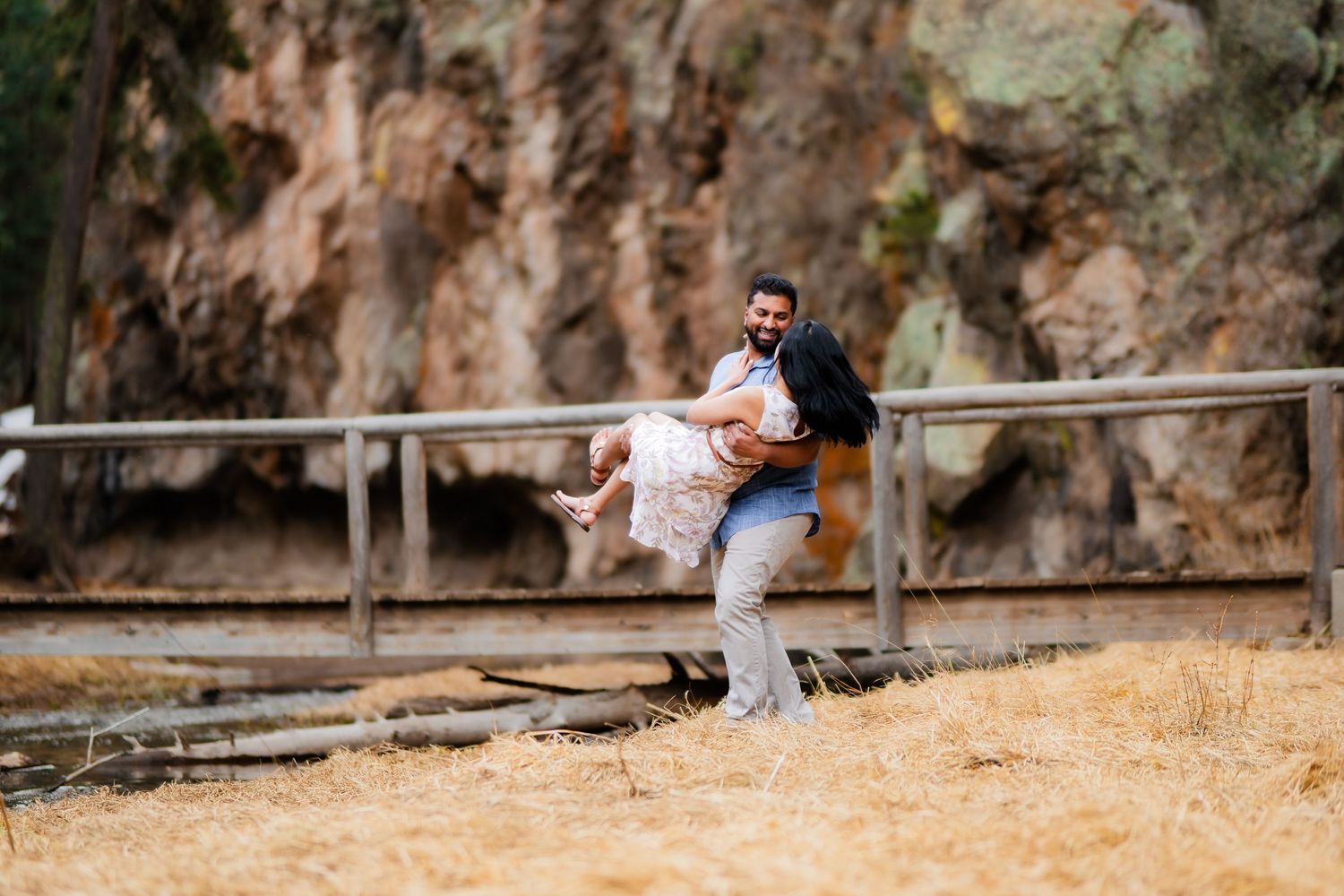 A playful moment captured on a wooden boardwalk with rocky cliffs in the background.