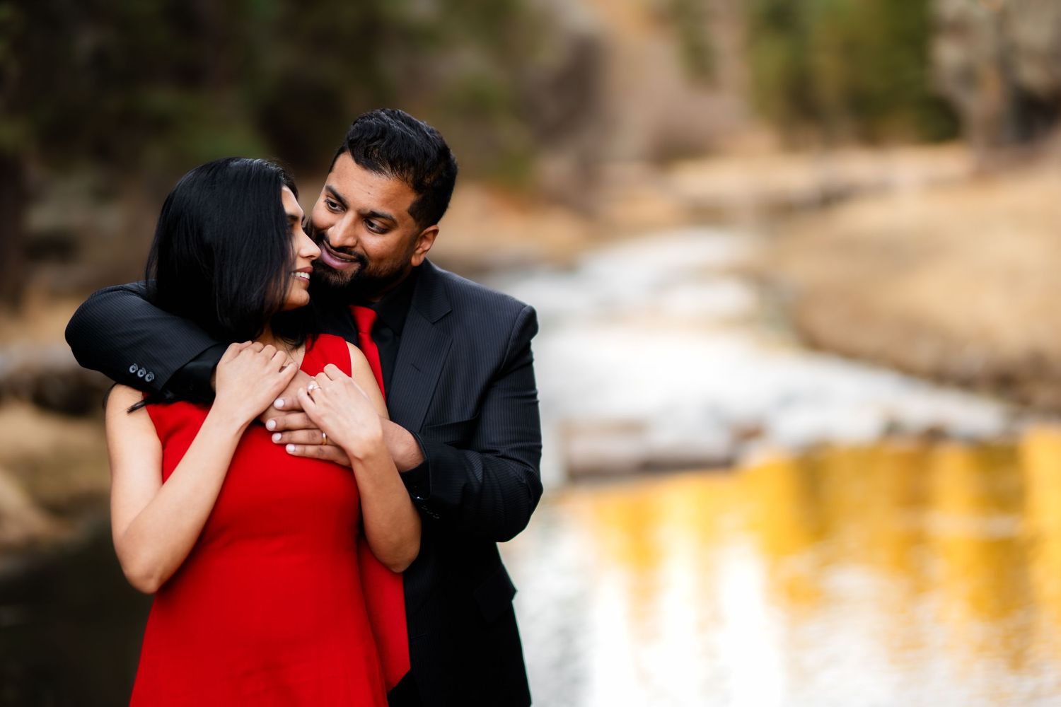 A couple embraces after their proposal by a scenic mountain lake with sunset lighting.
