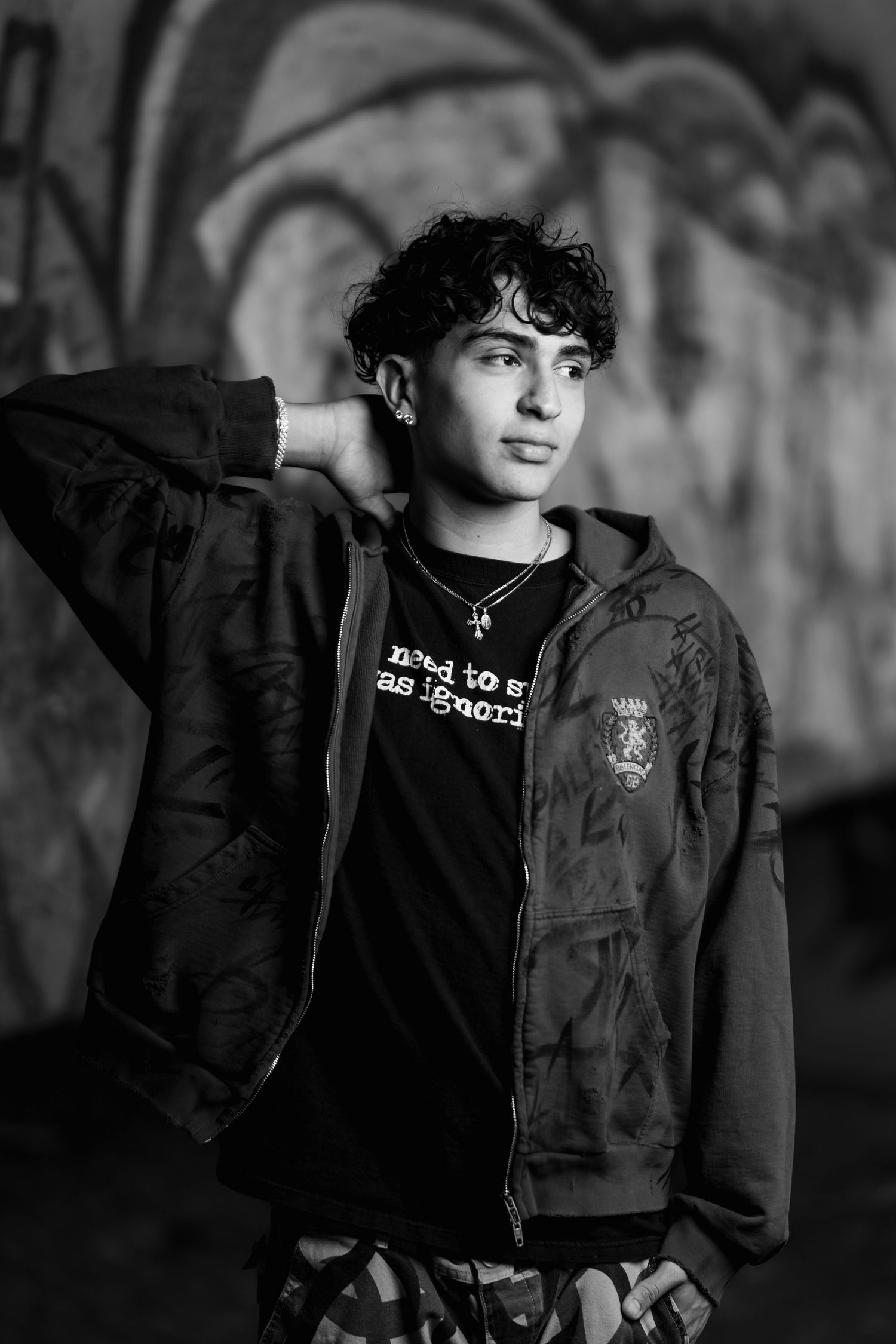 Black and white portrait shot capturing moody urban aesthetic with graffiti wall backdrop.