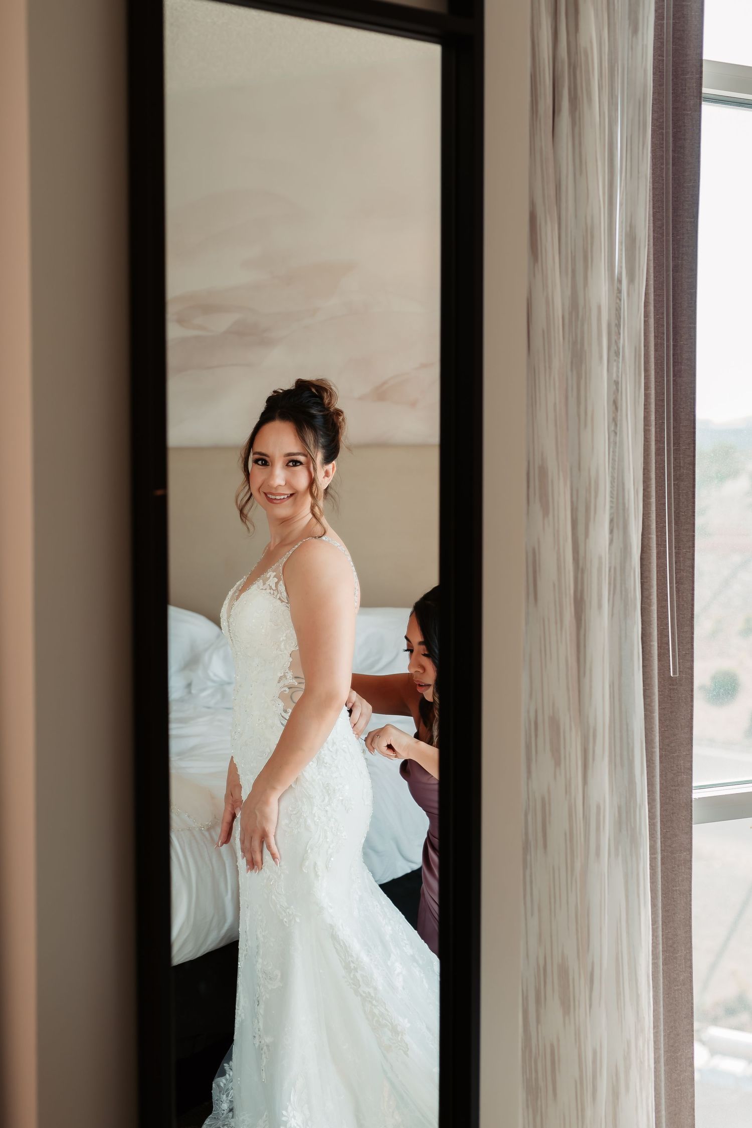 A wedding dress twirls gracefully in a sunlit room with floor-length windows.