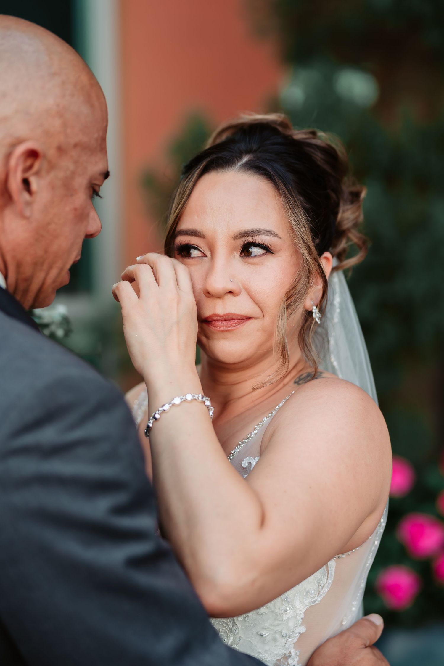 An emotional wedding scene outside a terracotta building with bright pink flowers in the background.