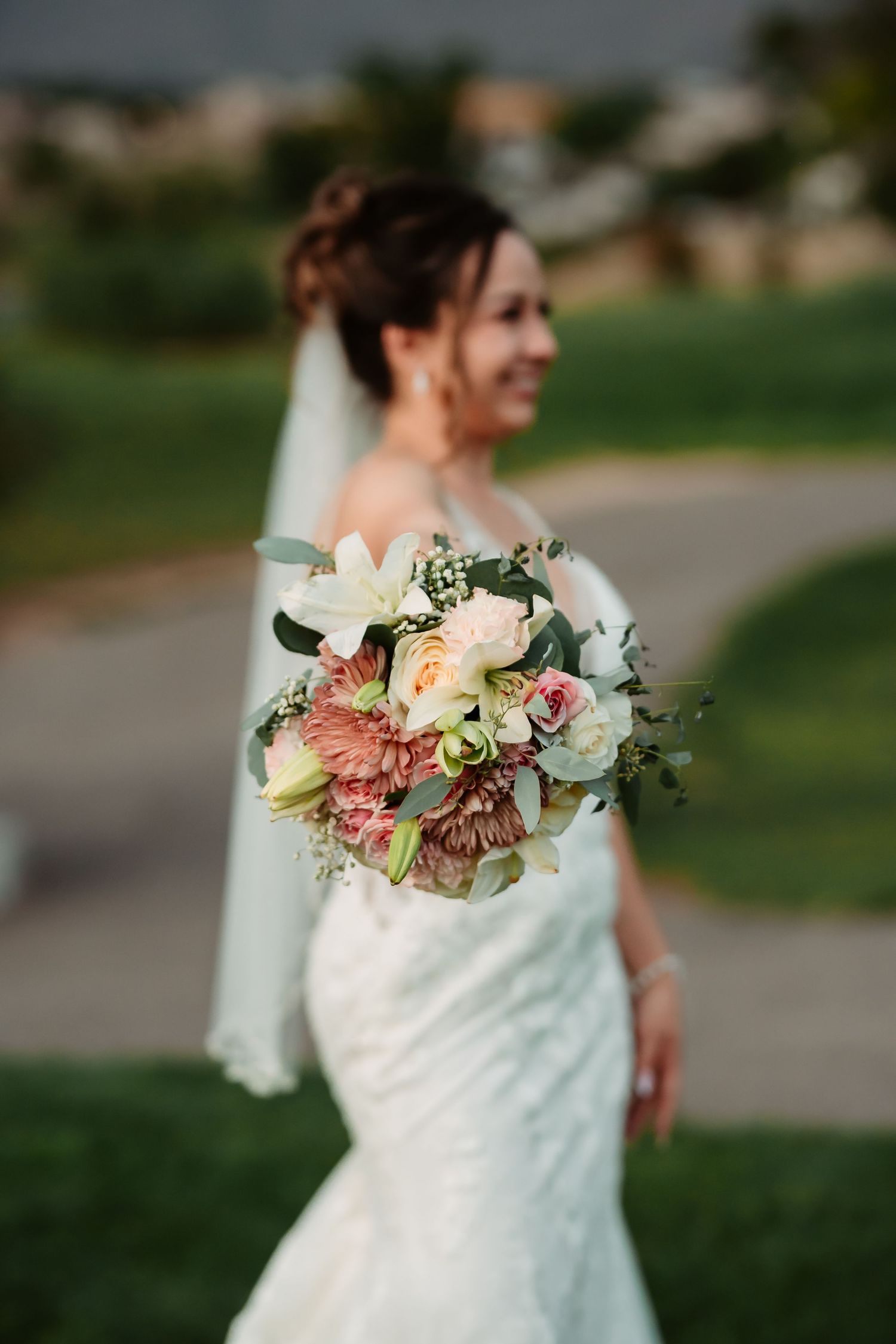 Joyful bride twirls in white lace wedding dress while holding a pink and white floral bouquet.