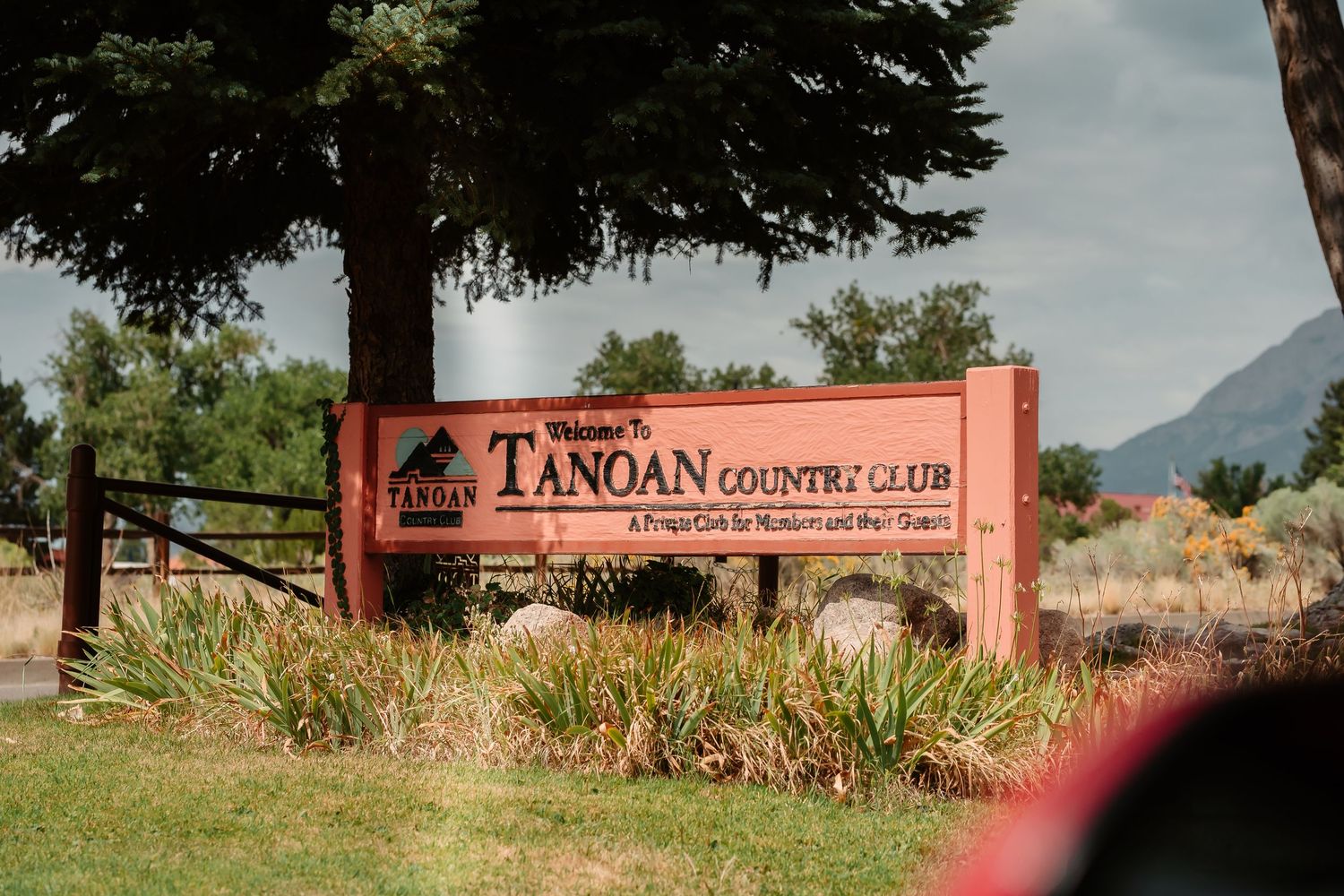 Scenic mountain landscape with rustic buildings and a country club sign in the background.