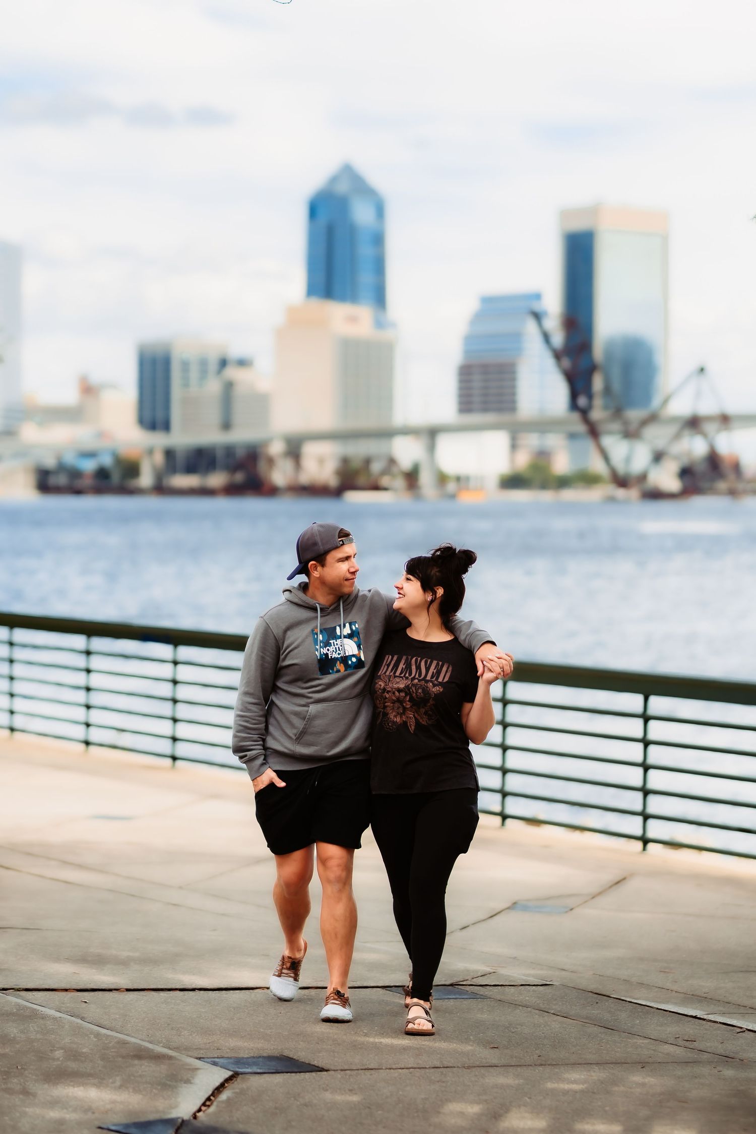 A couple shares a romantic moment along Jacksonville's riverfront with the city skyline in the background.