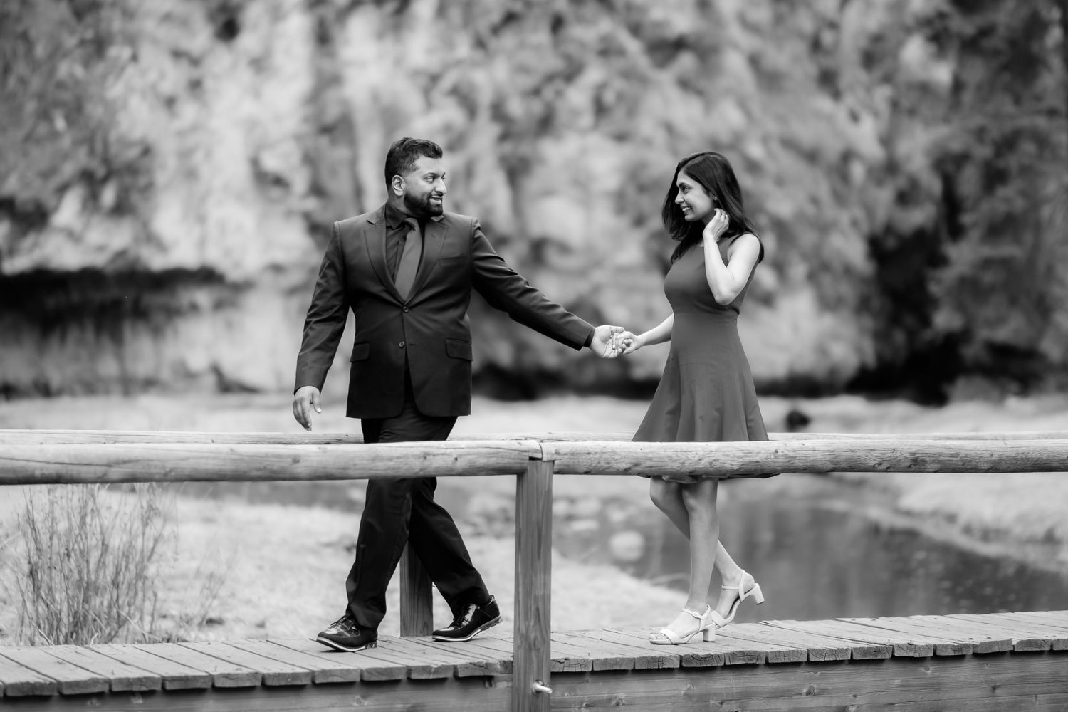 A black and white photo of a couple sharing a moment on a wooden walkway by water.