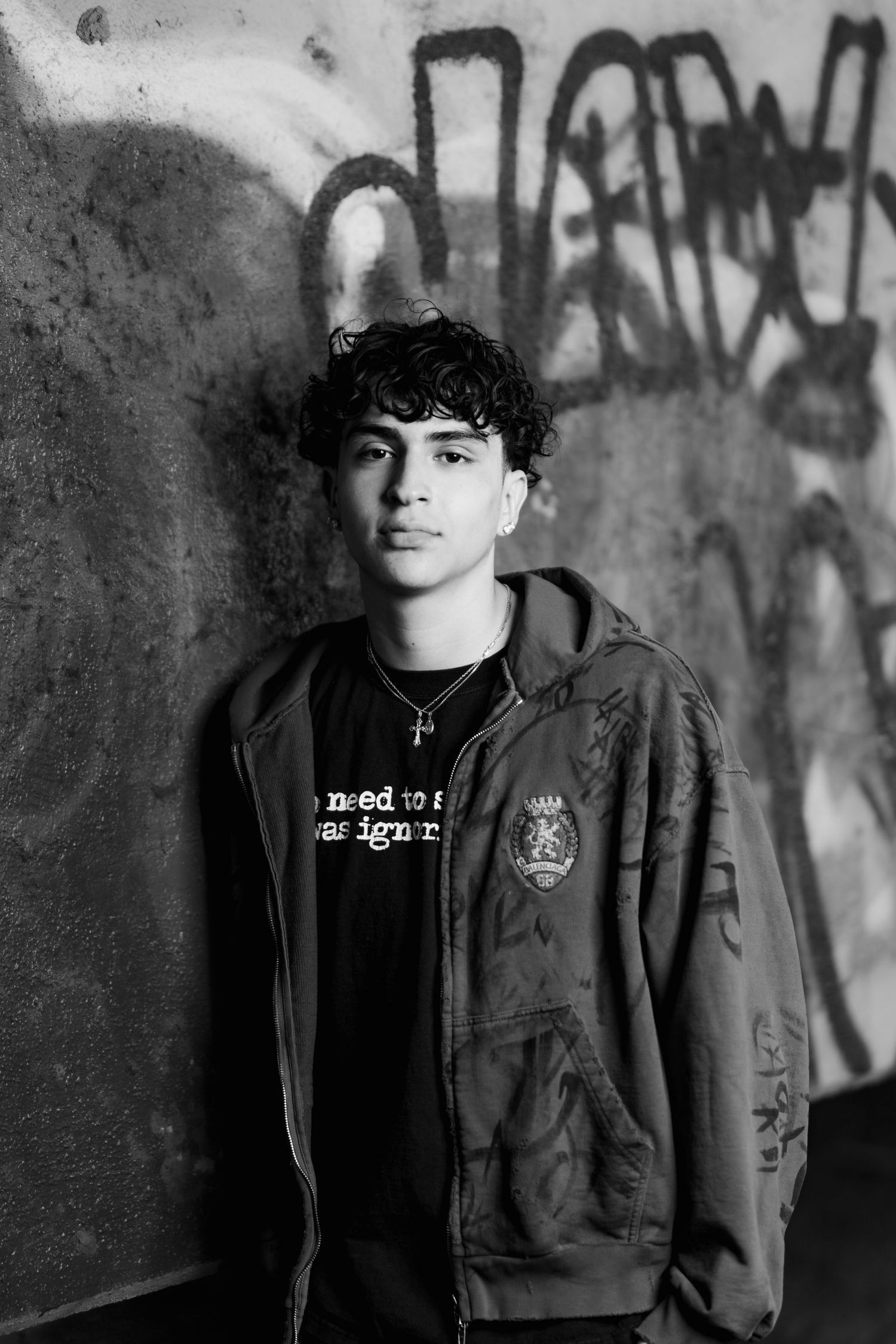 Monochrome portrait of person in casual wear against graffiti wall.