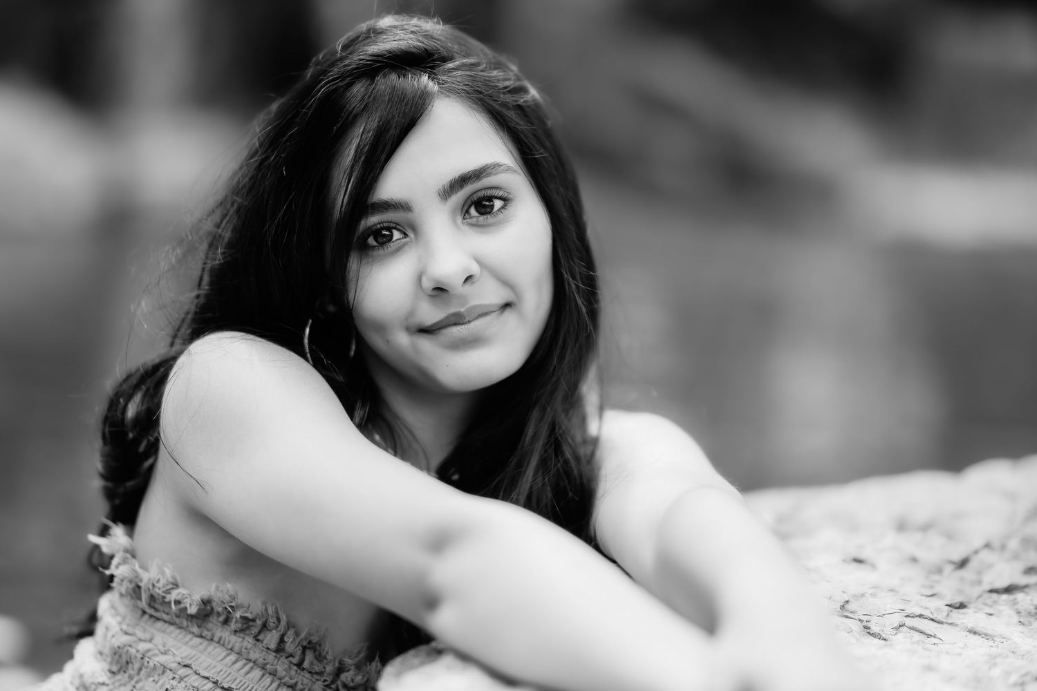 Black and white portrait of a young woman with long dark hair leaning on a surface while looking at camera.