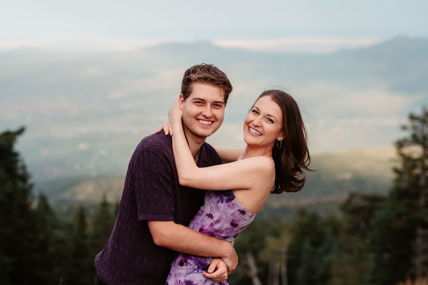 A couple shares a tender moment against a mountain backdrop.