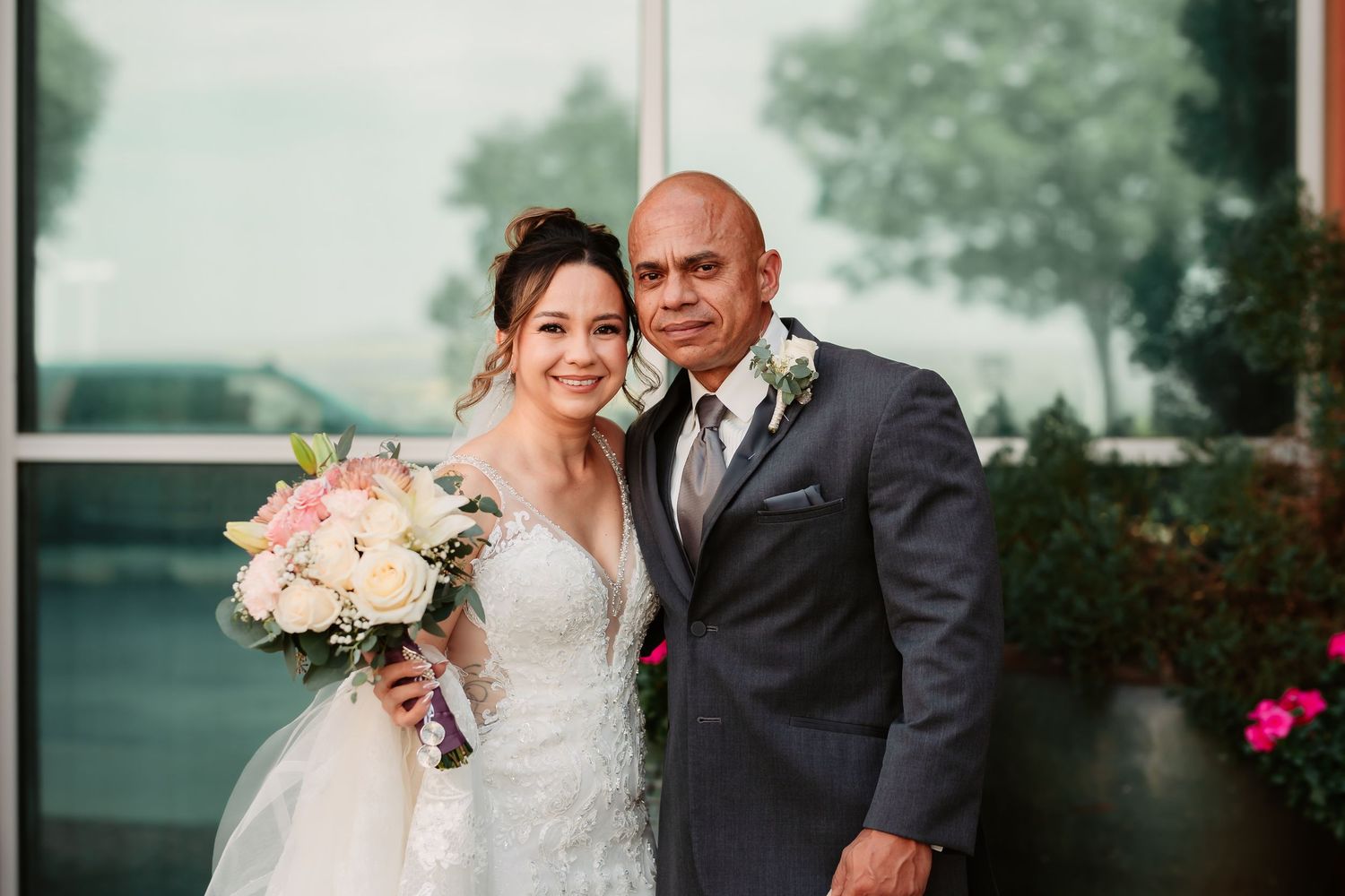 A romantic wedding photo of a couple embracing outdoors with the bride holding a pink and white floral bouquet.