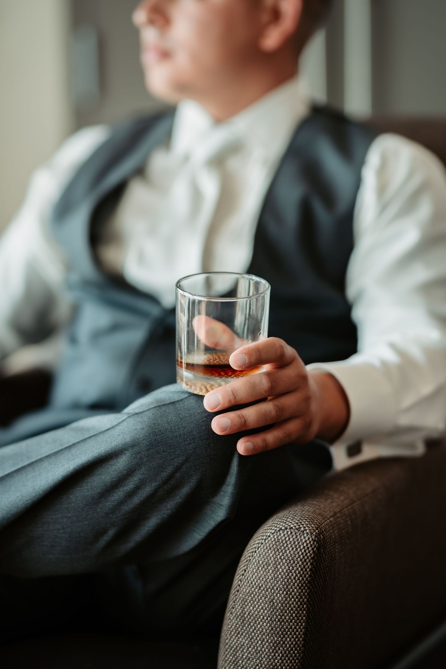Close-up shots of hands holding a glass of whiskey while seated on a grey couch.