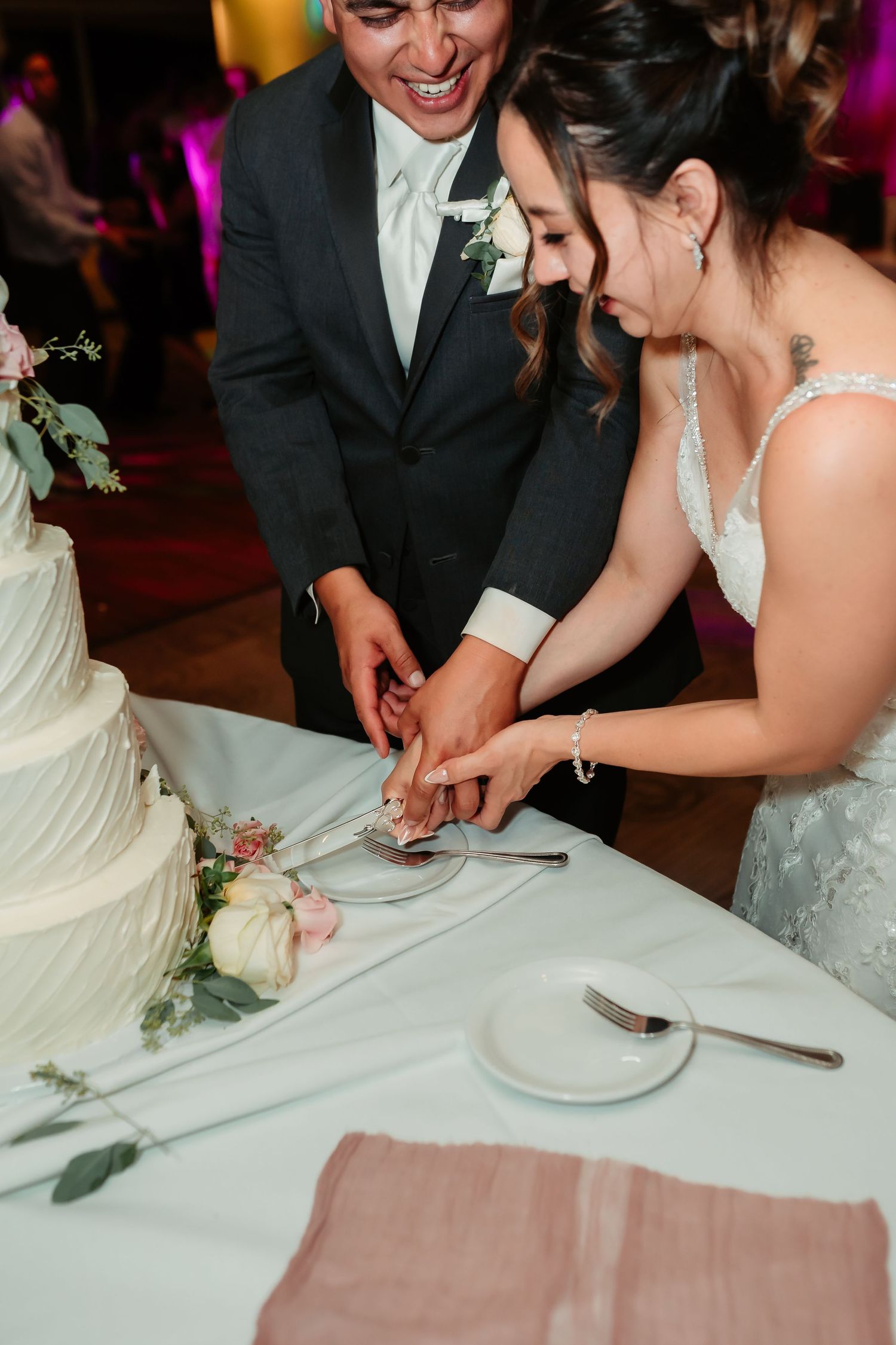 A couple cuts into their elegant white wedding cake decorated with fresh flowers.