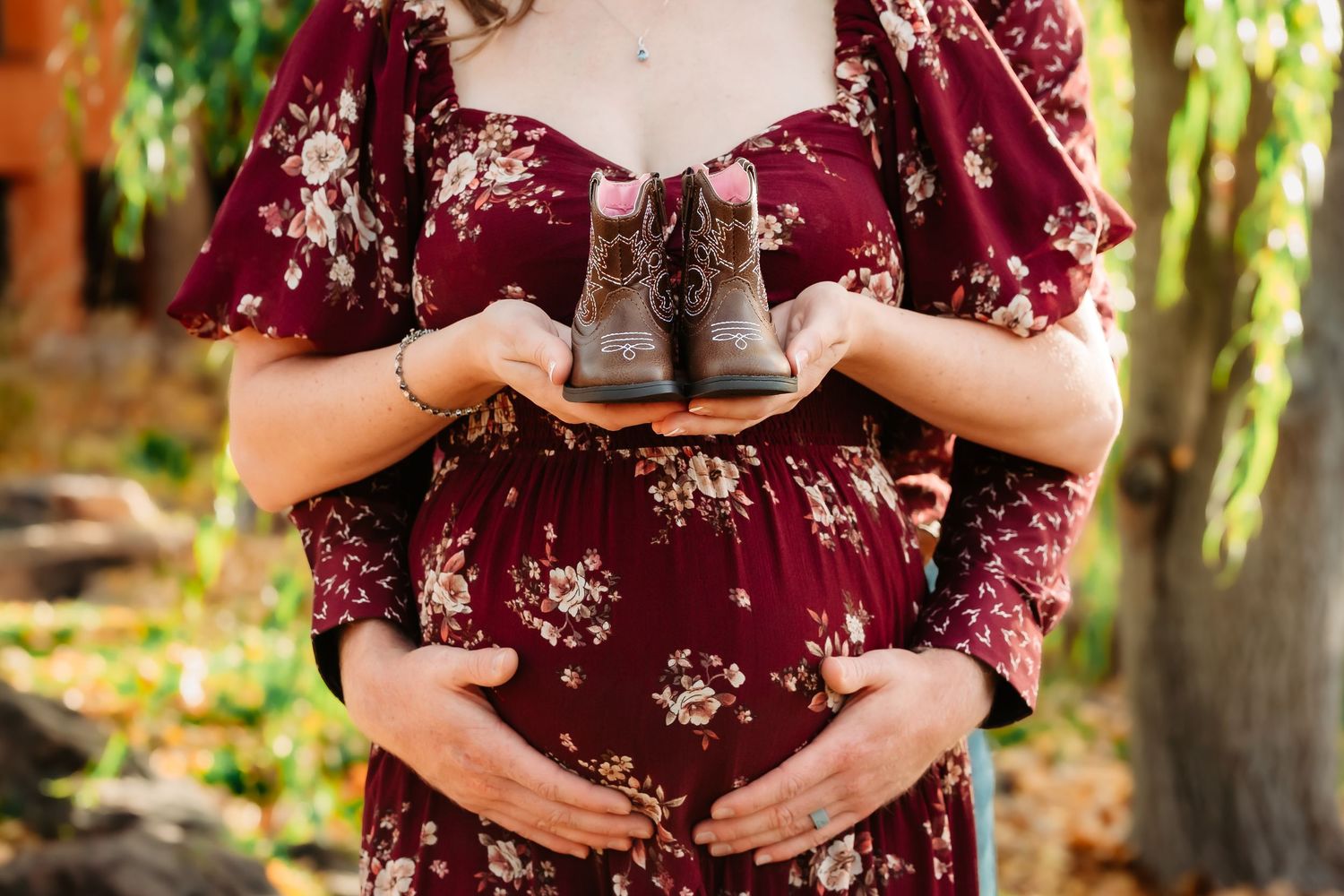 A burgundy floral maternity dress is shown in multiple poses against a sunlit outdoor garden backdrop.