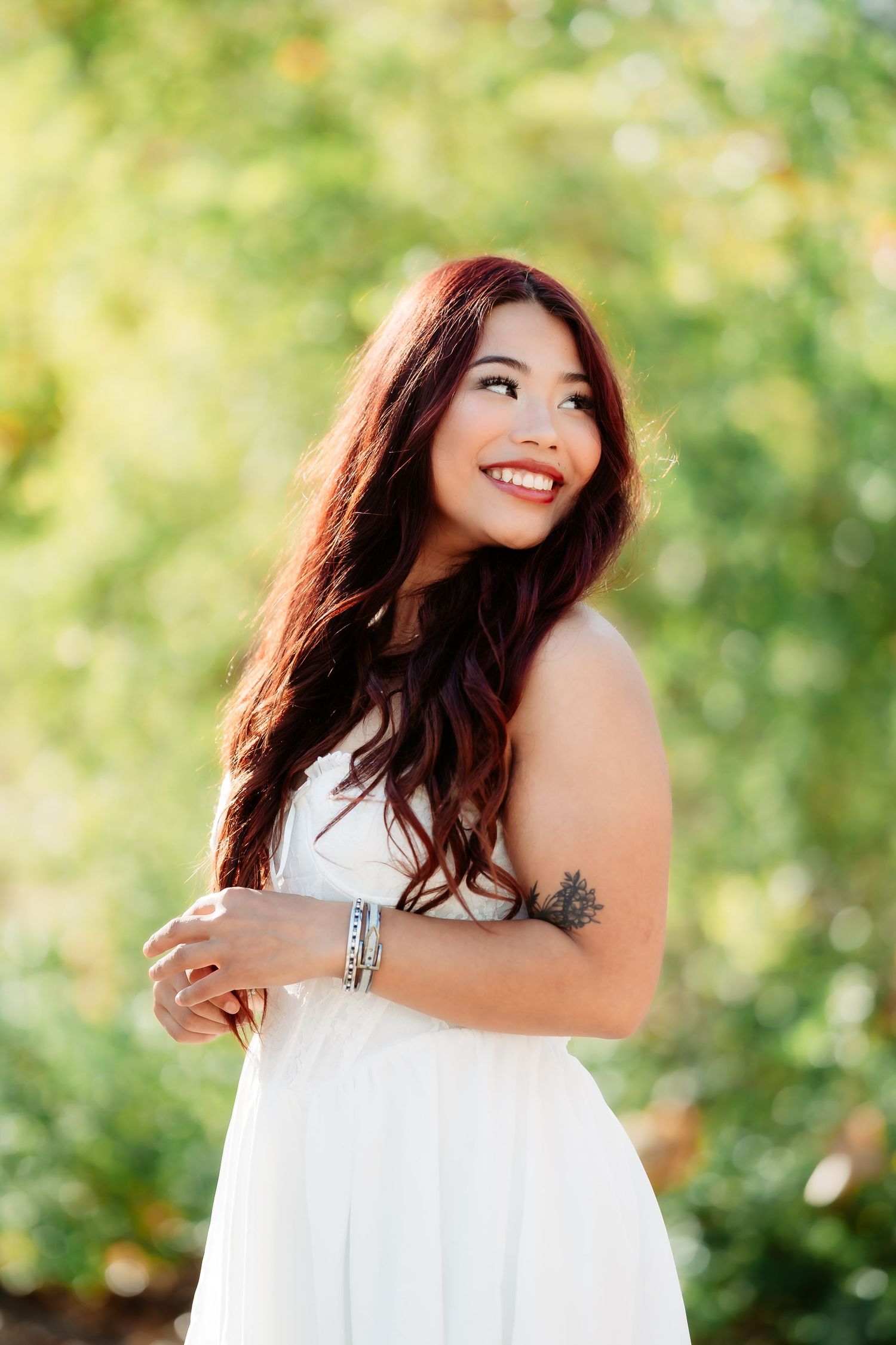 A person in a flowing white dress poses gracefully against a soft green natural backdrop.