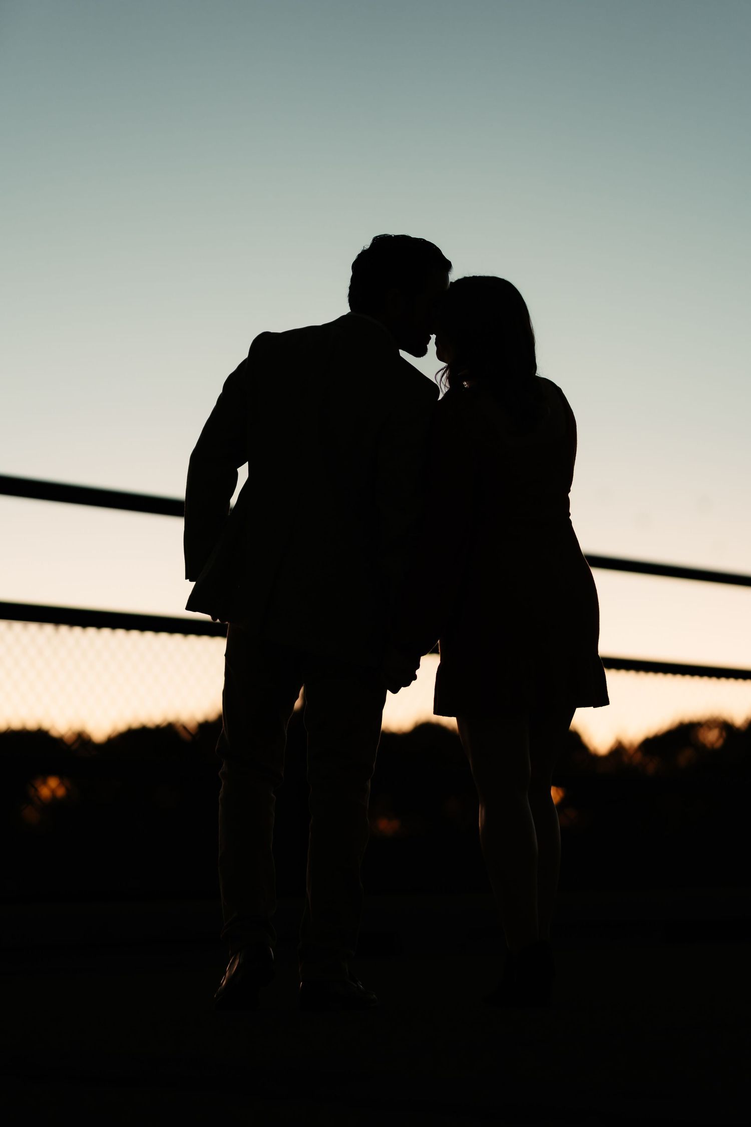 Silhouettes of two people kissing against a sunset sky with a dark horizon line.