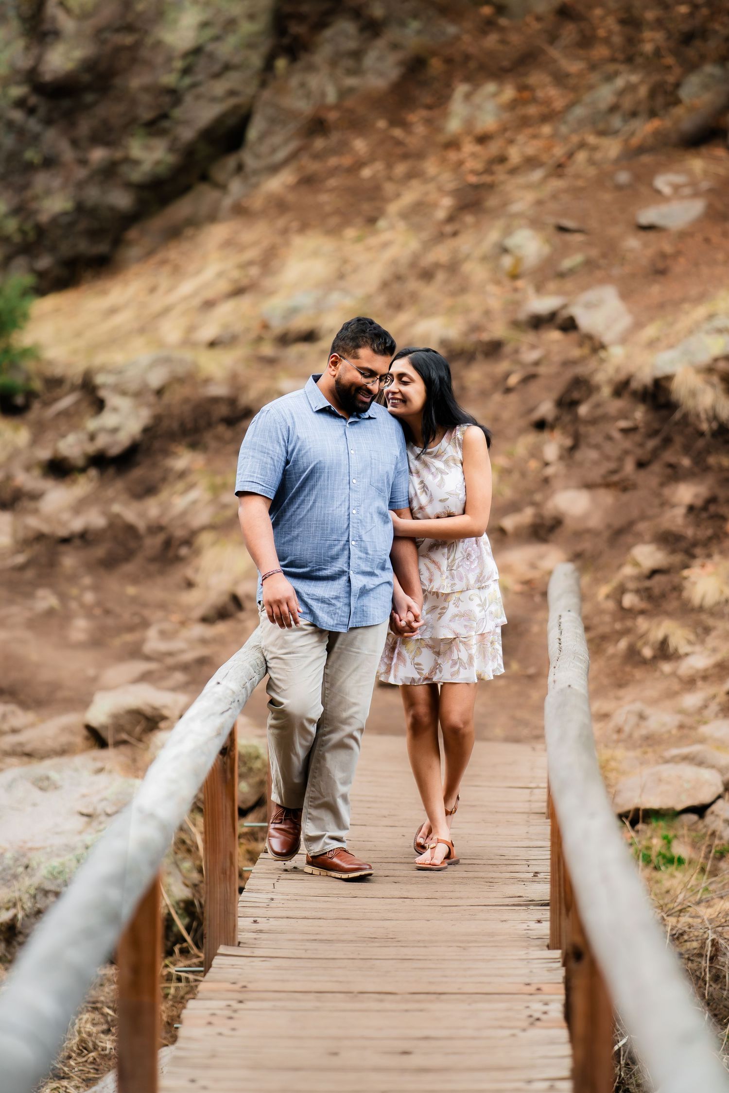 A couple shares an intimate moment while walking on a wooden boardwalk in nature.