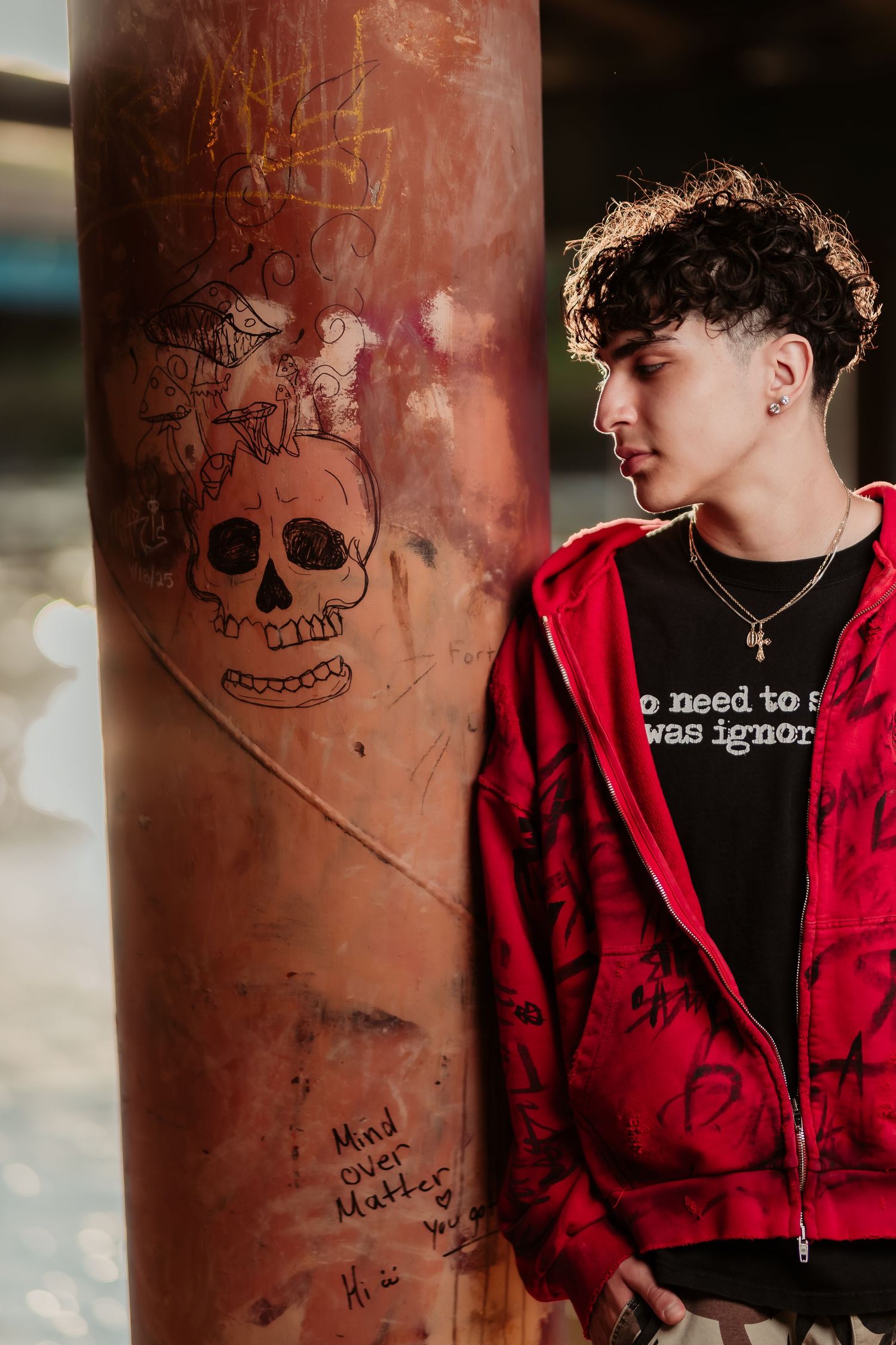Portrait next to graffiti wall with skull drawing wearing red jacket and black shirt.
