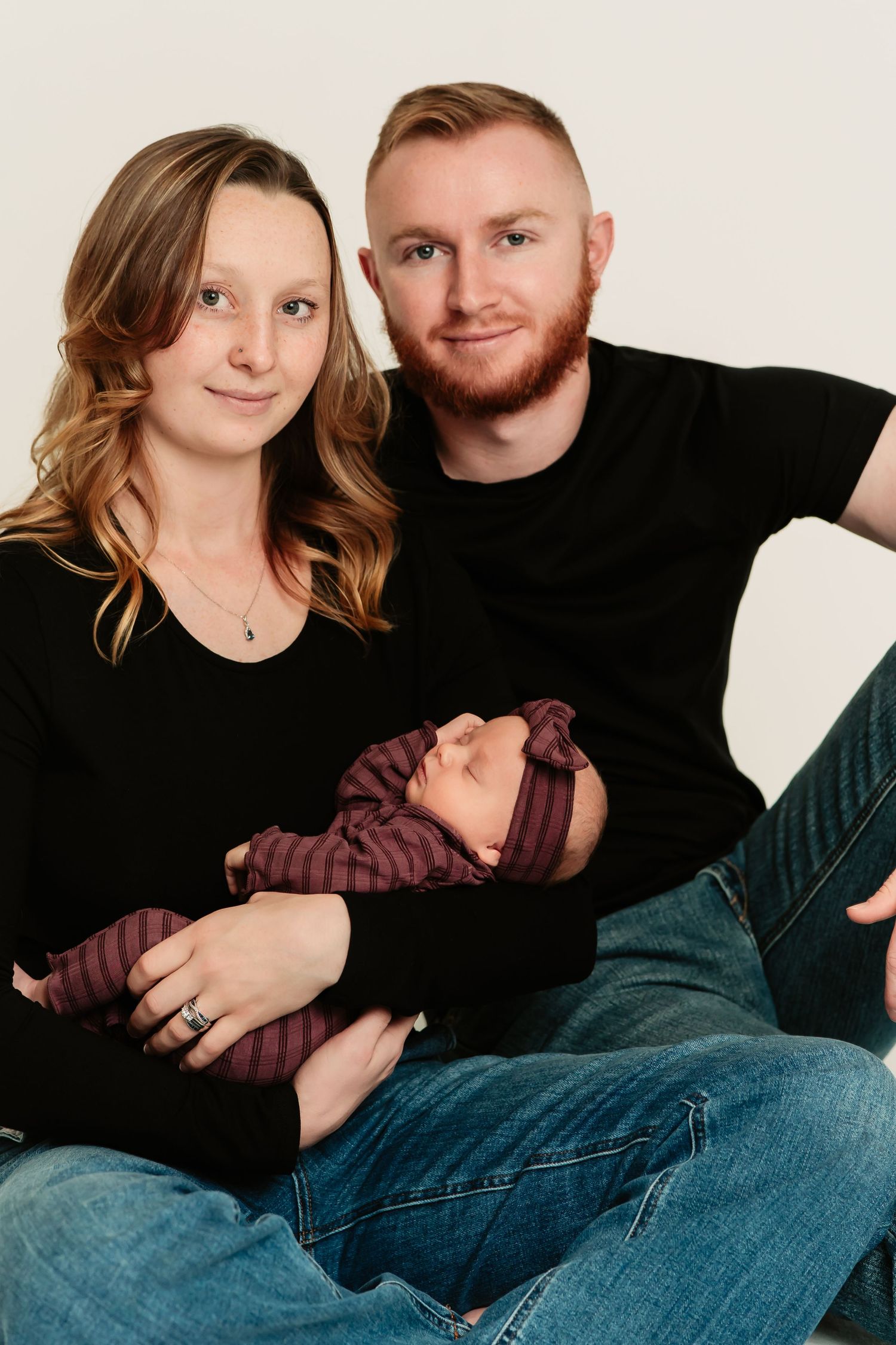 A couple in casual attire poses together on a light background in a series of intimate portrait photos.