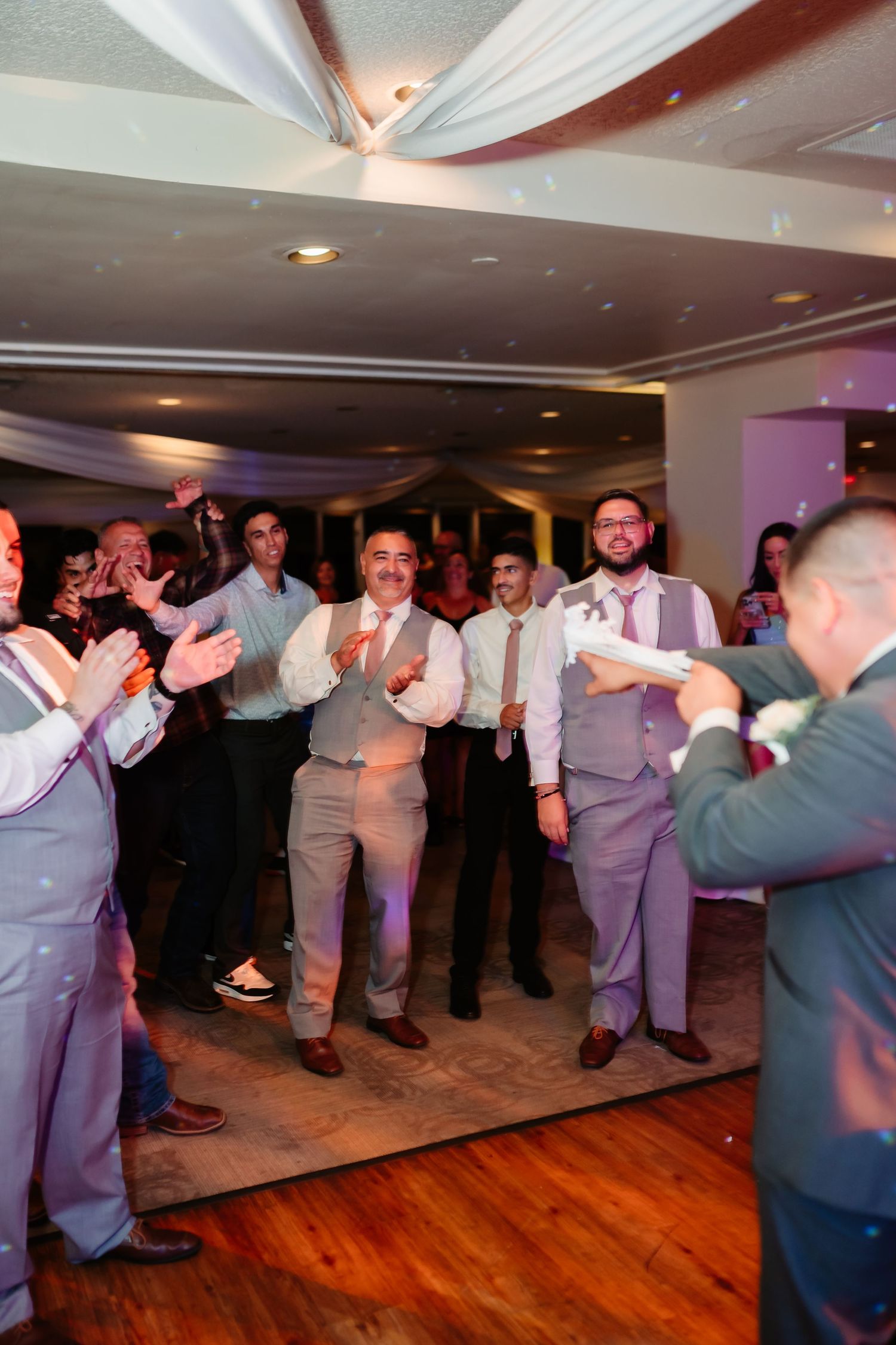 Large group of wedding guests dancing in coordinated formation at an indoor reception venue.