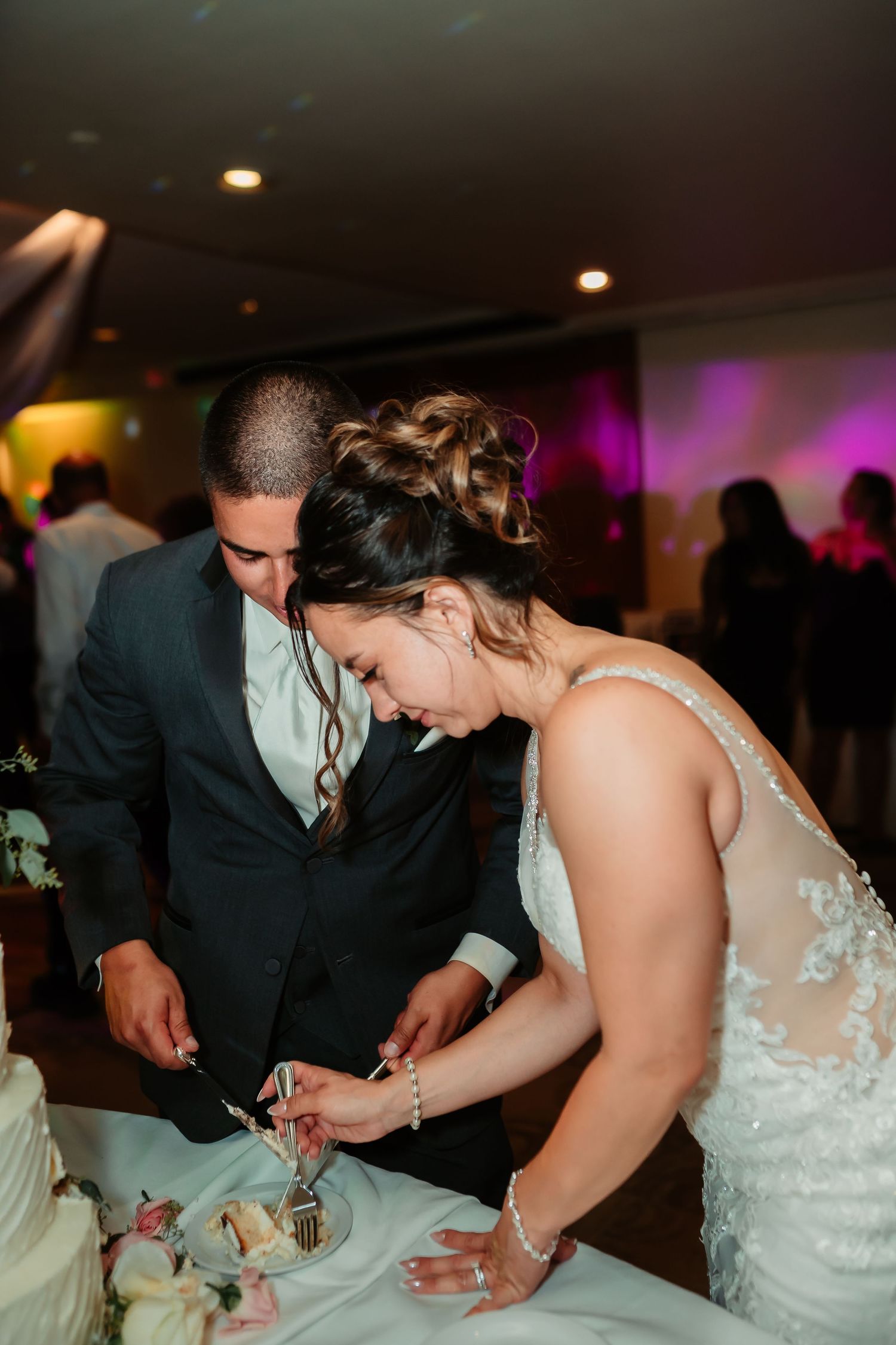 A couple in formal wedding attire participates in a traditional wedding cake cutting ceremony at their reception.