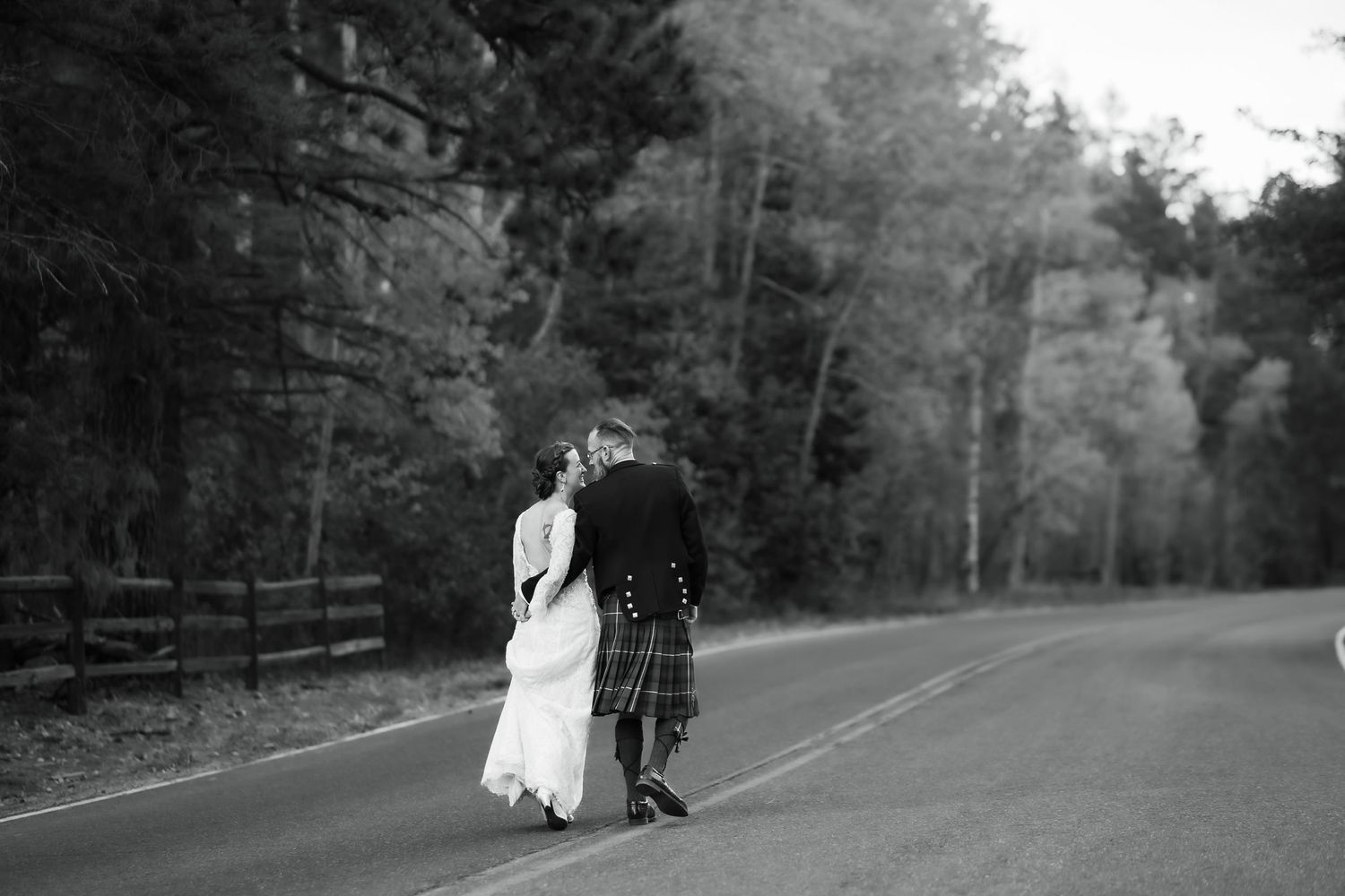 A romantic couple walking down a tree-lined path in black and white photography.