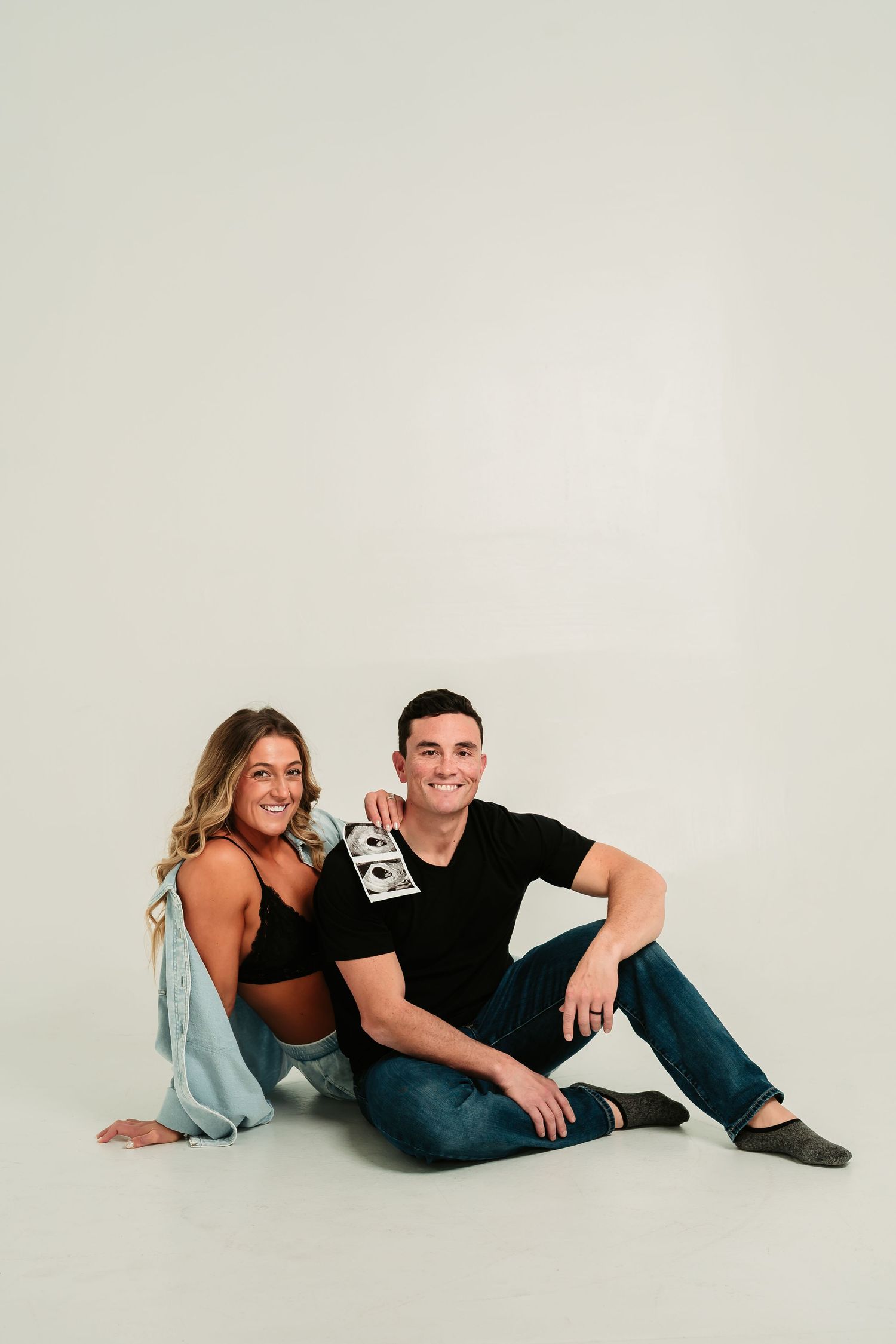 A couple poses together in a casual photo series on a white background wearing black and blue outfits.