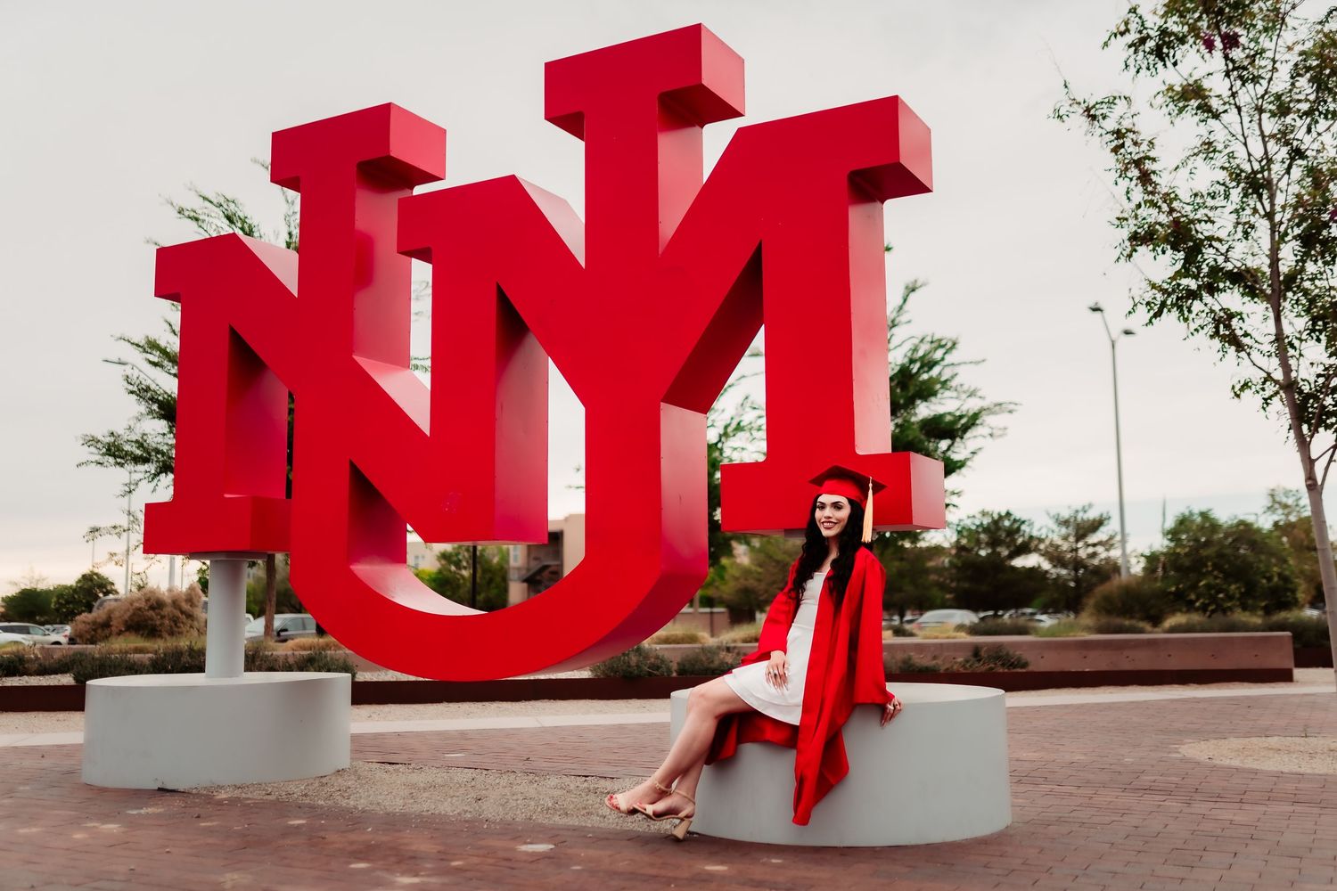 A series of bright red sculptural letters arranged in a modern outdoor installation against a cloudy sky.