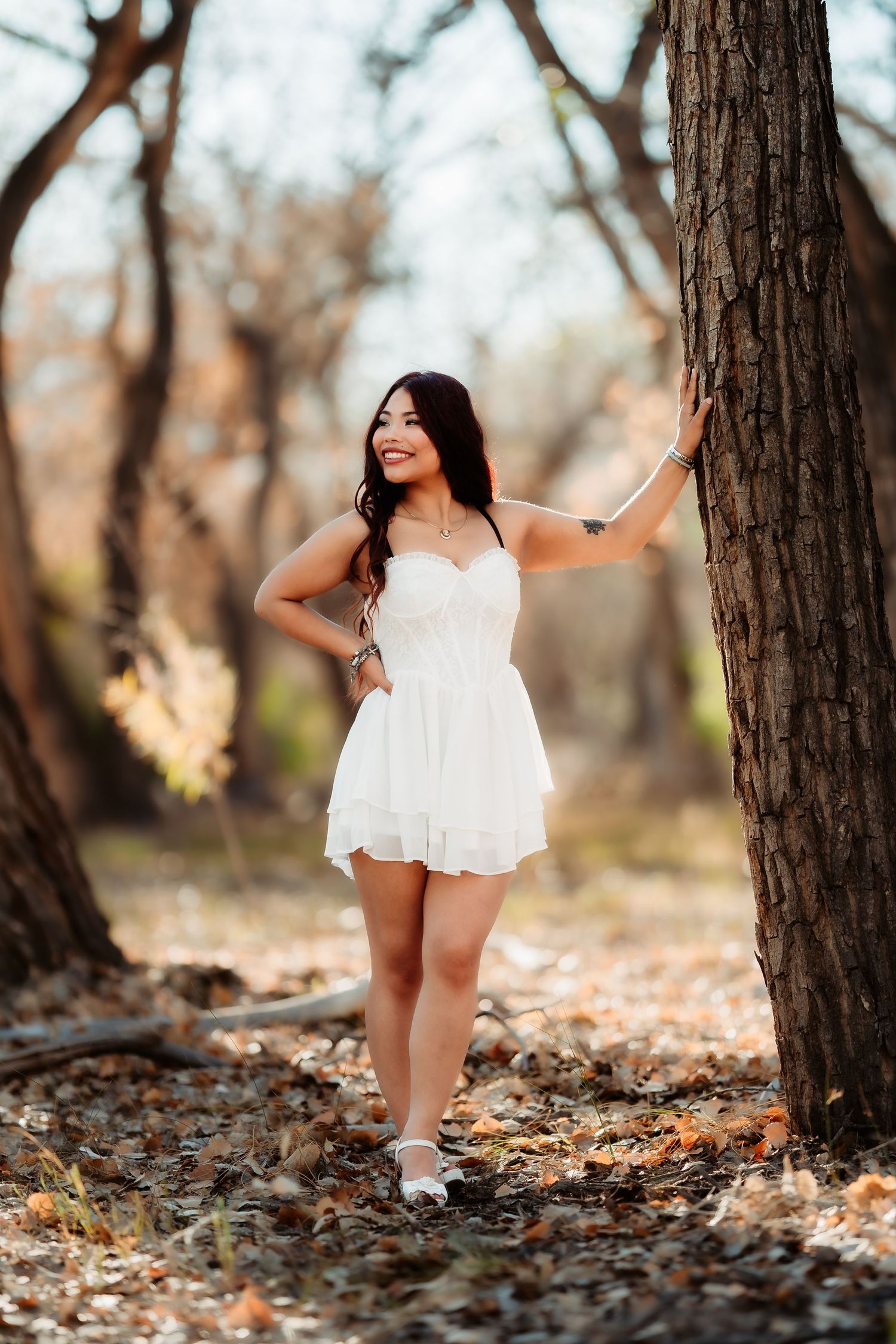 White dress contrasts against fallen autumn leaves in artistic outdoor portrait.