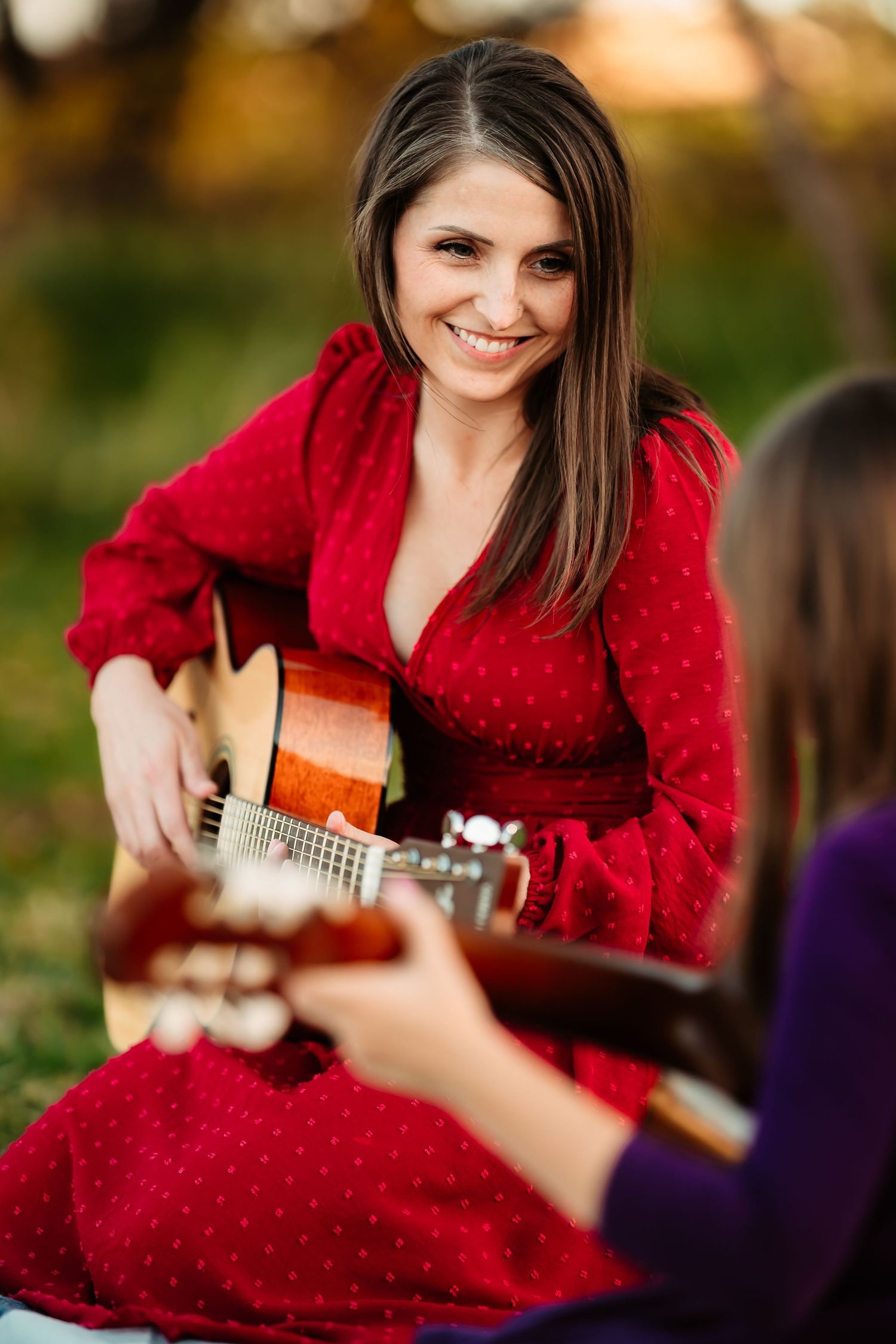 A musician in a vibrant red sweater plays acoustic guitar outdoors during an autumn photo session.