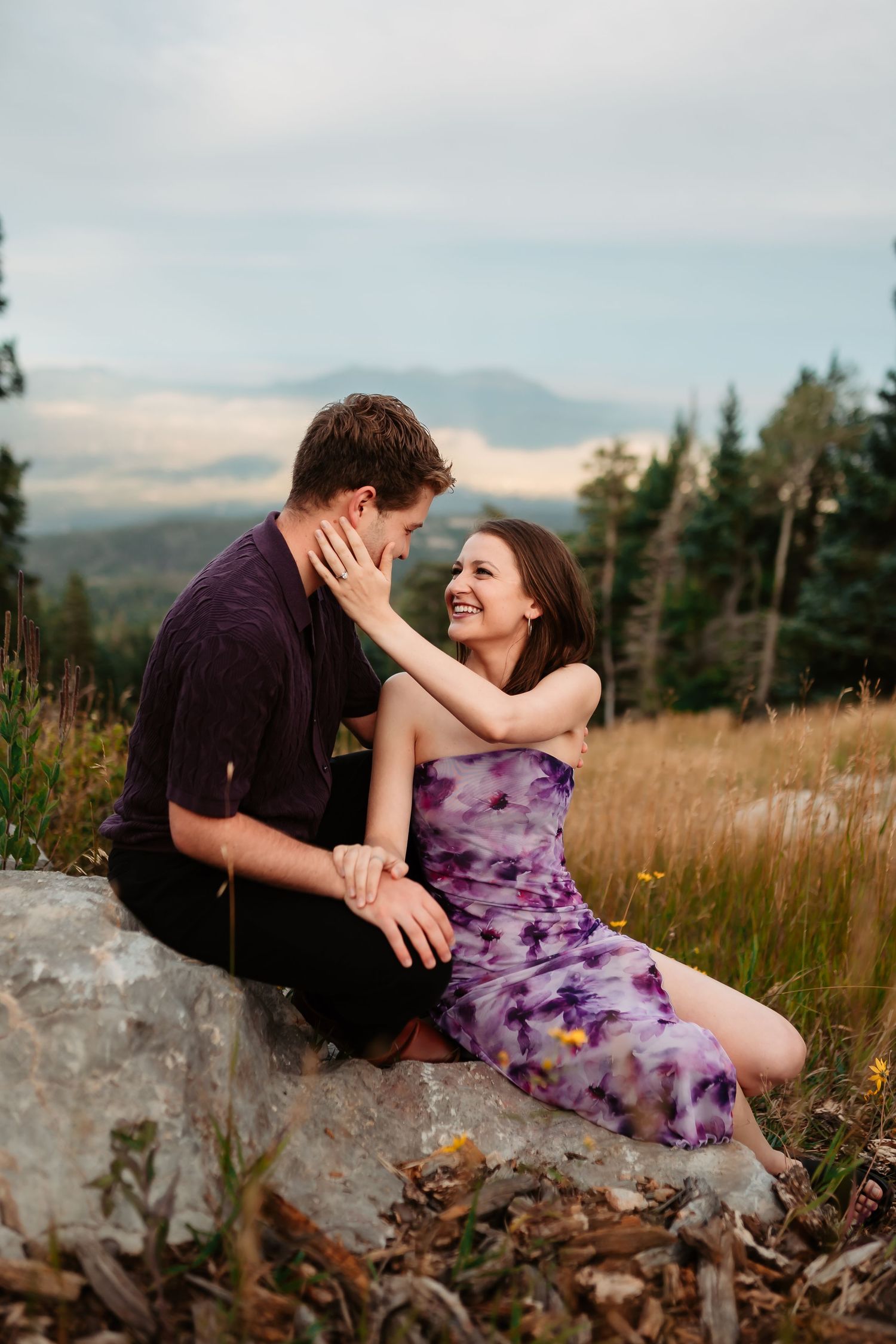 Intimate moment captured on a rocky mountain overlook with purple wildflowers and evergreen forest.