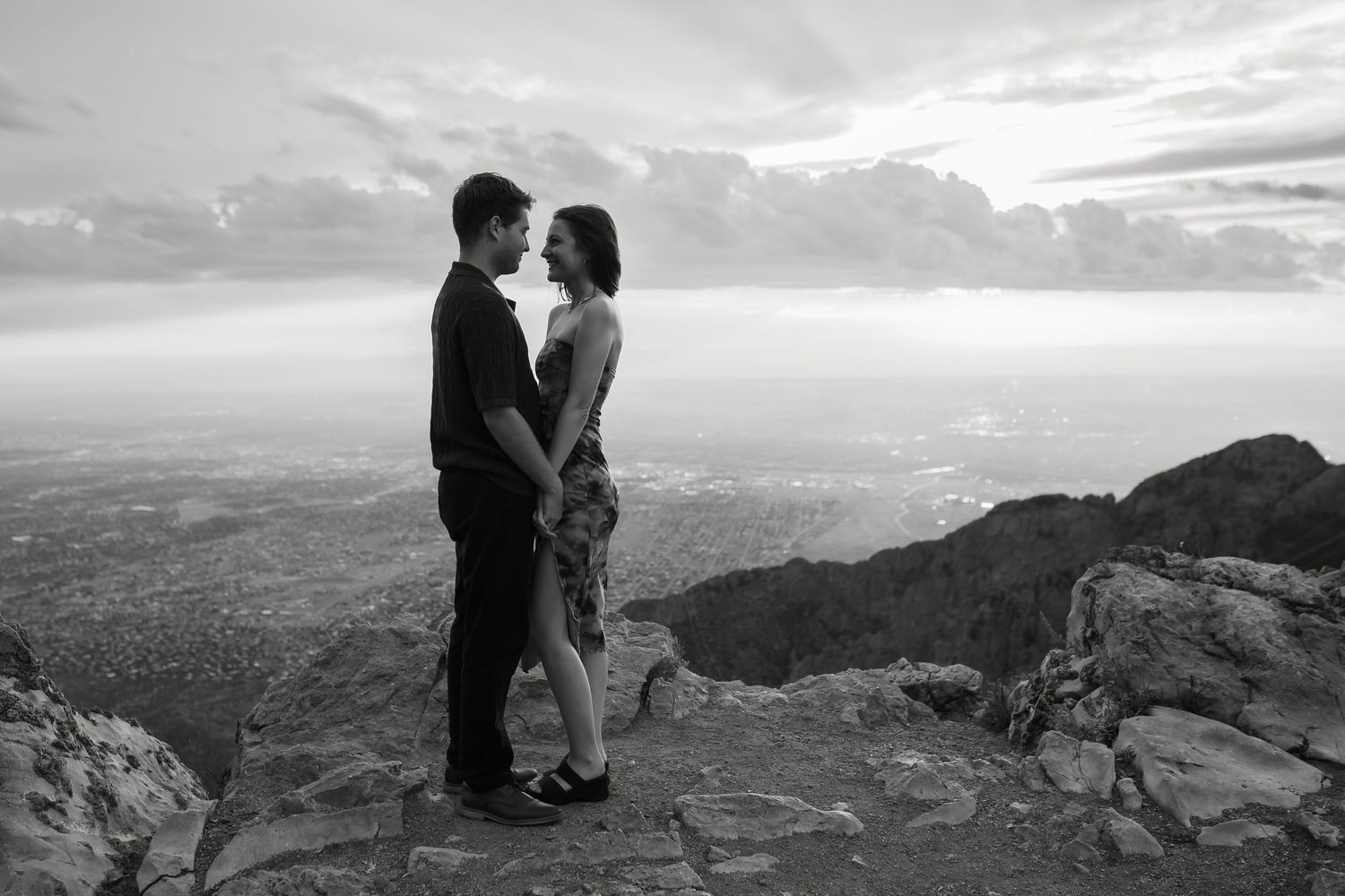 Black and white panoramic of couple embracing on dramatic rocky mountain overlook.