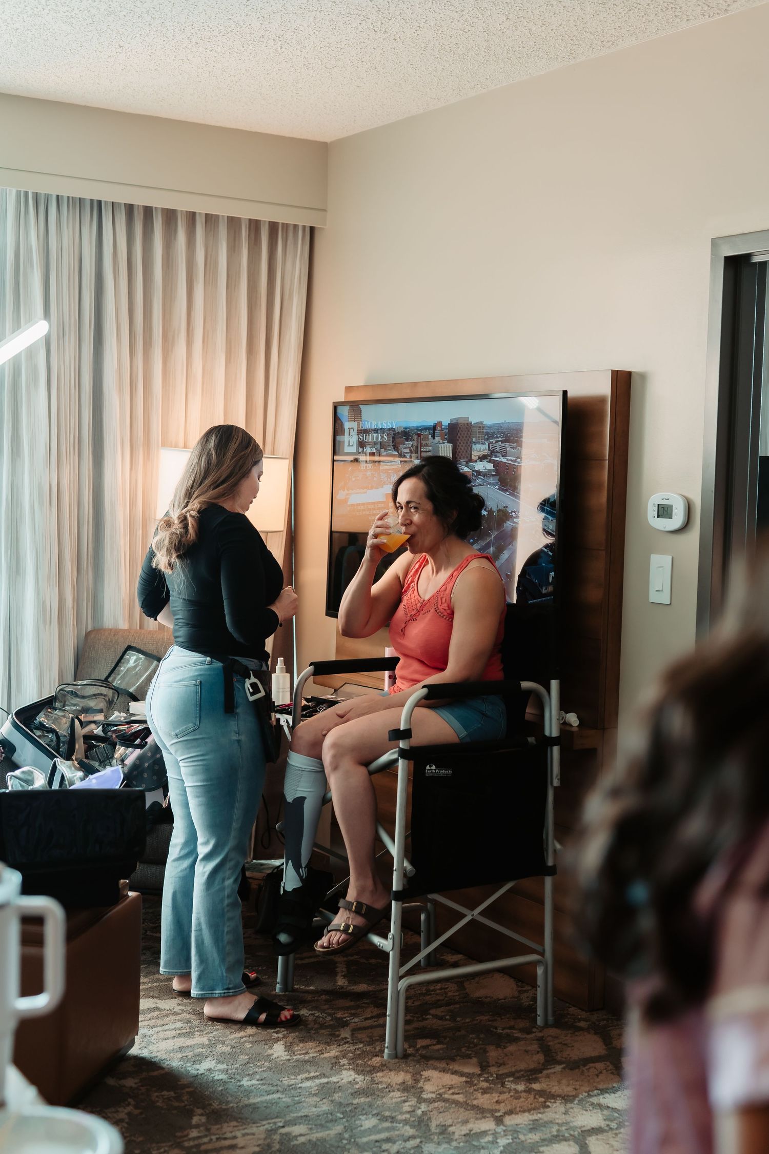 Multiple people sit in chairs while getting ready in a hotel room for a wedding event.