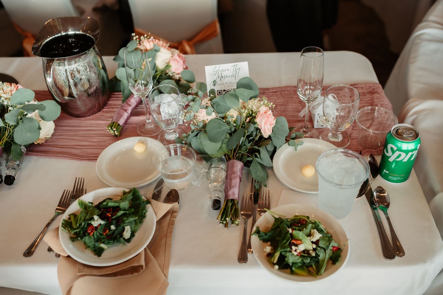 Elegant place settings with white floral centerpieces and greenery at a wedding reception.