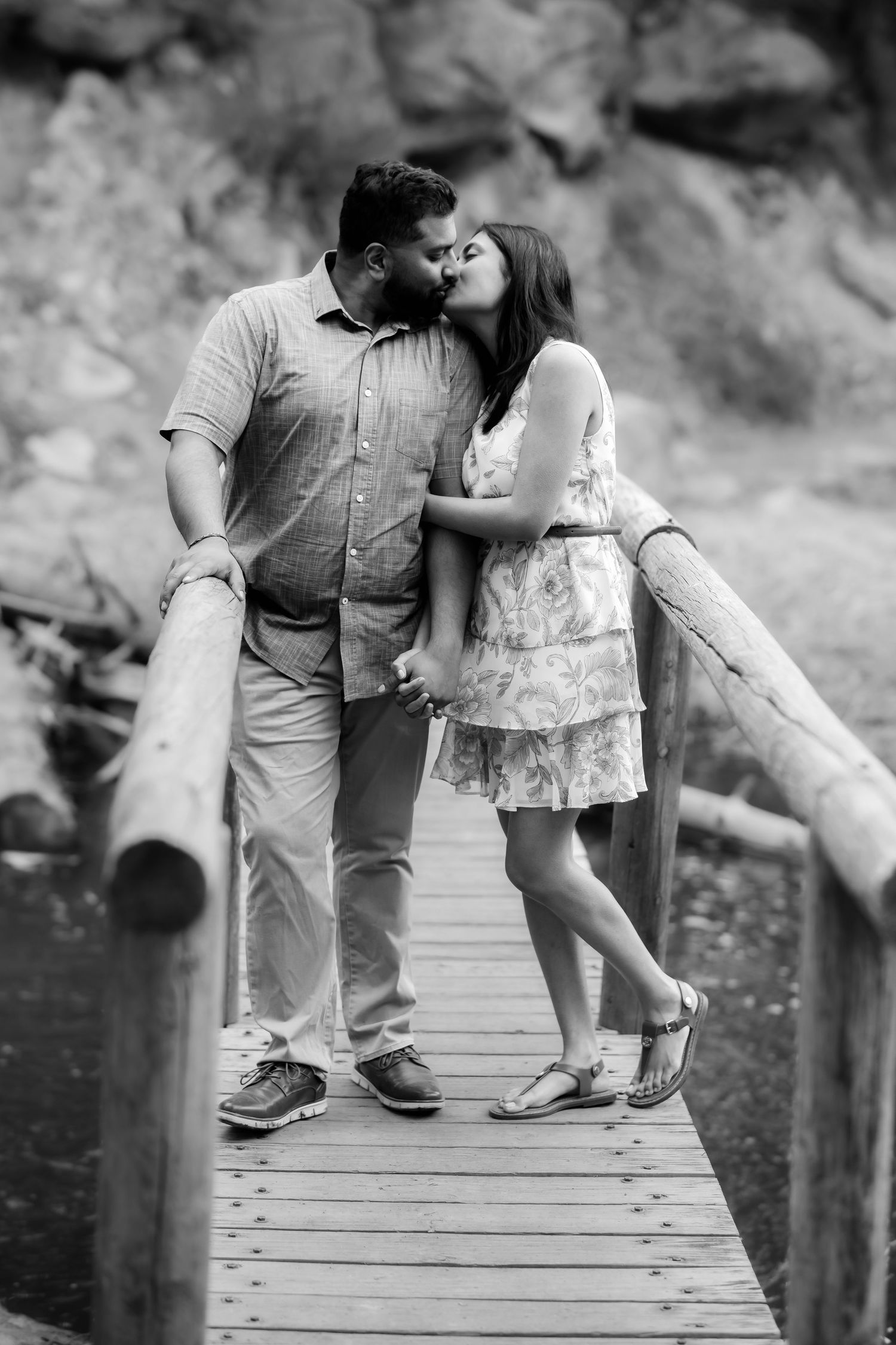 A couple shares a tender kiss on a wooden bridge in black and white photography.