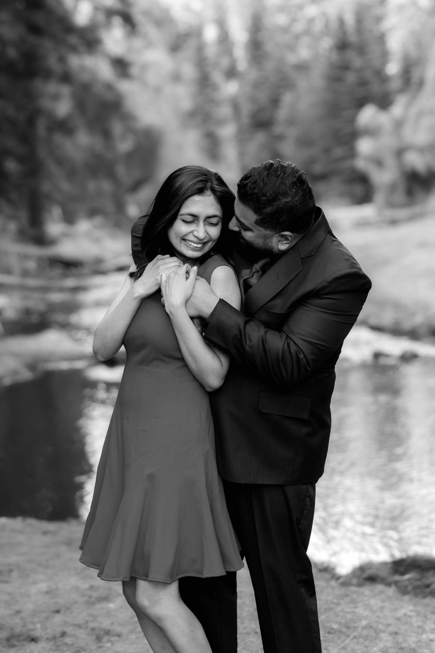 A black and white photo of a couple sharing an intimate moment by a lake.