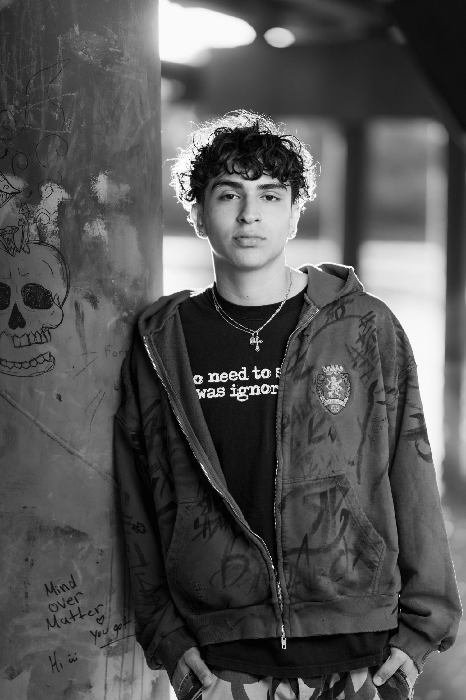 Black and white artistic shot of person in hooded jacket with street art and skull graffiti visible in background.