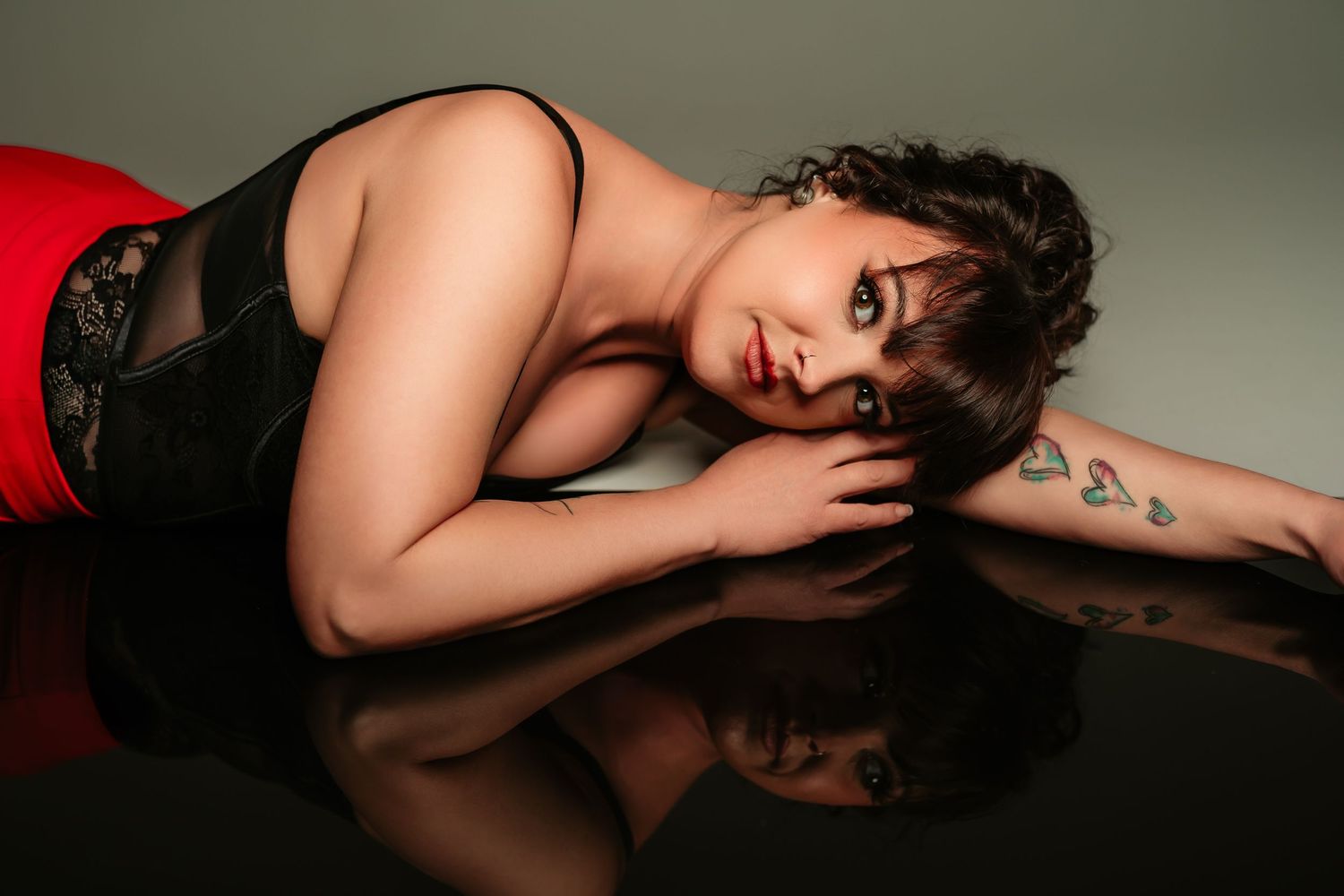 Person in black lingerie poses seductively on light colored background in artistic boudoir photoshoot.