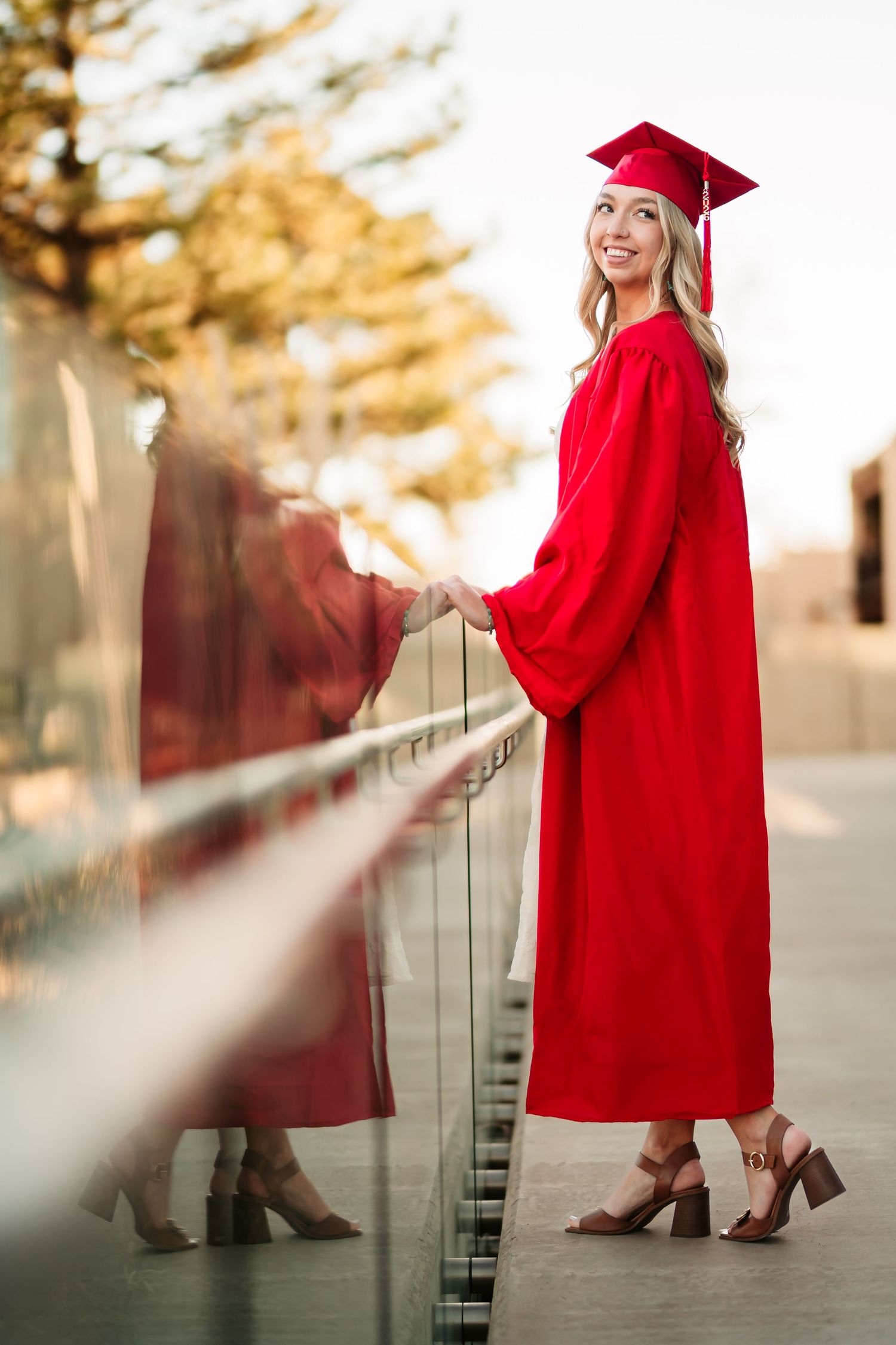 Graduate in red cap and gown poses on outdoor steps during golden hour sunset for graduation photos.