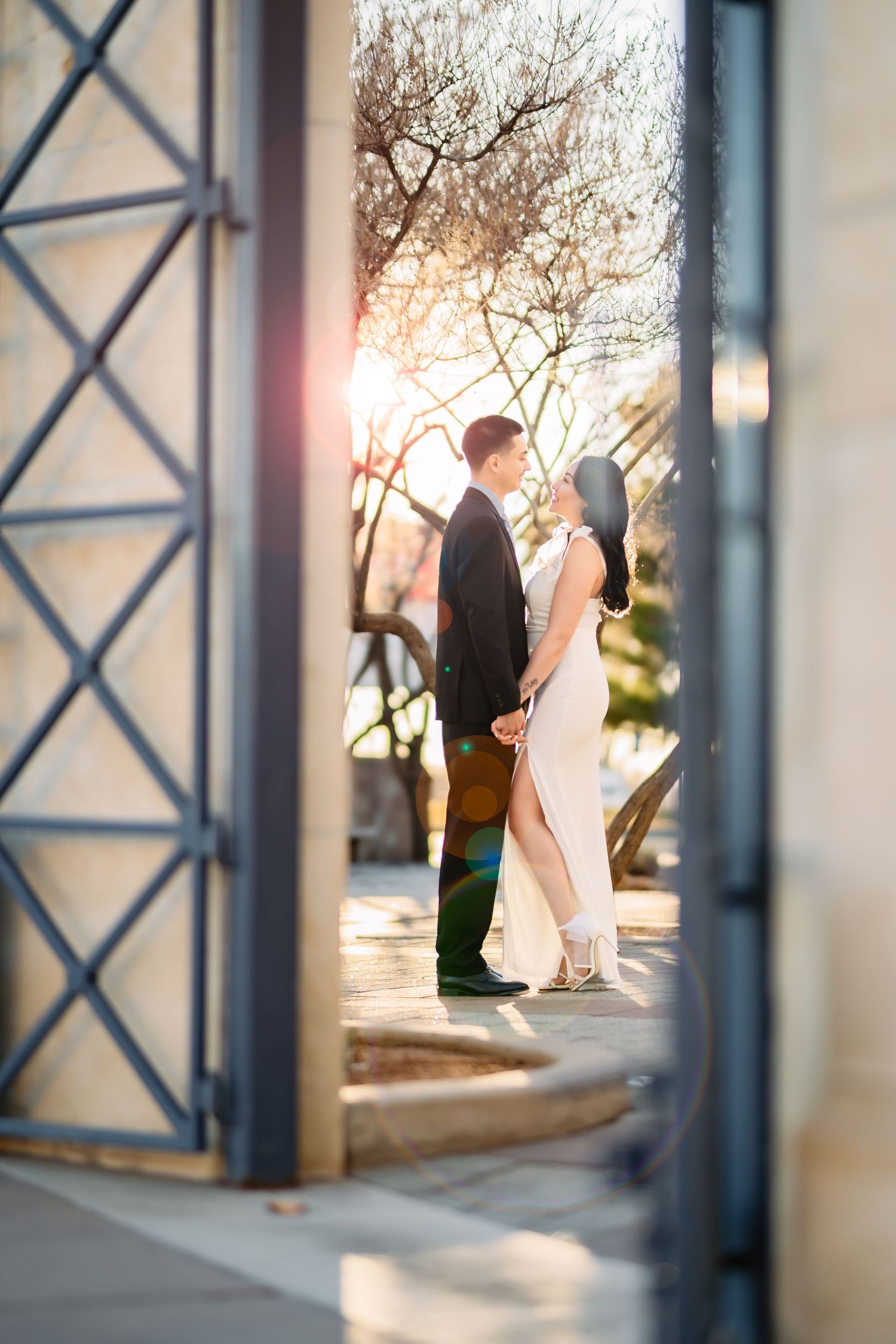 Romantic wedding couple shares an intimate moment at sunset through architectural columns in an outdoor setting.