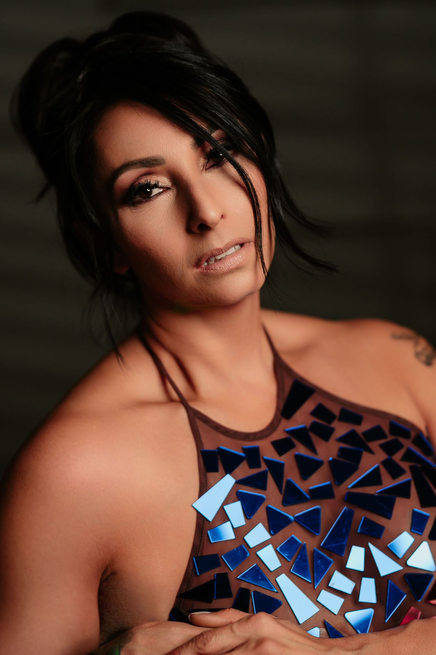 A person wearing a shimmering blue geometric patterned dress poses against a dark background.