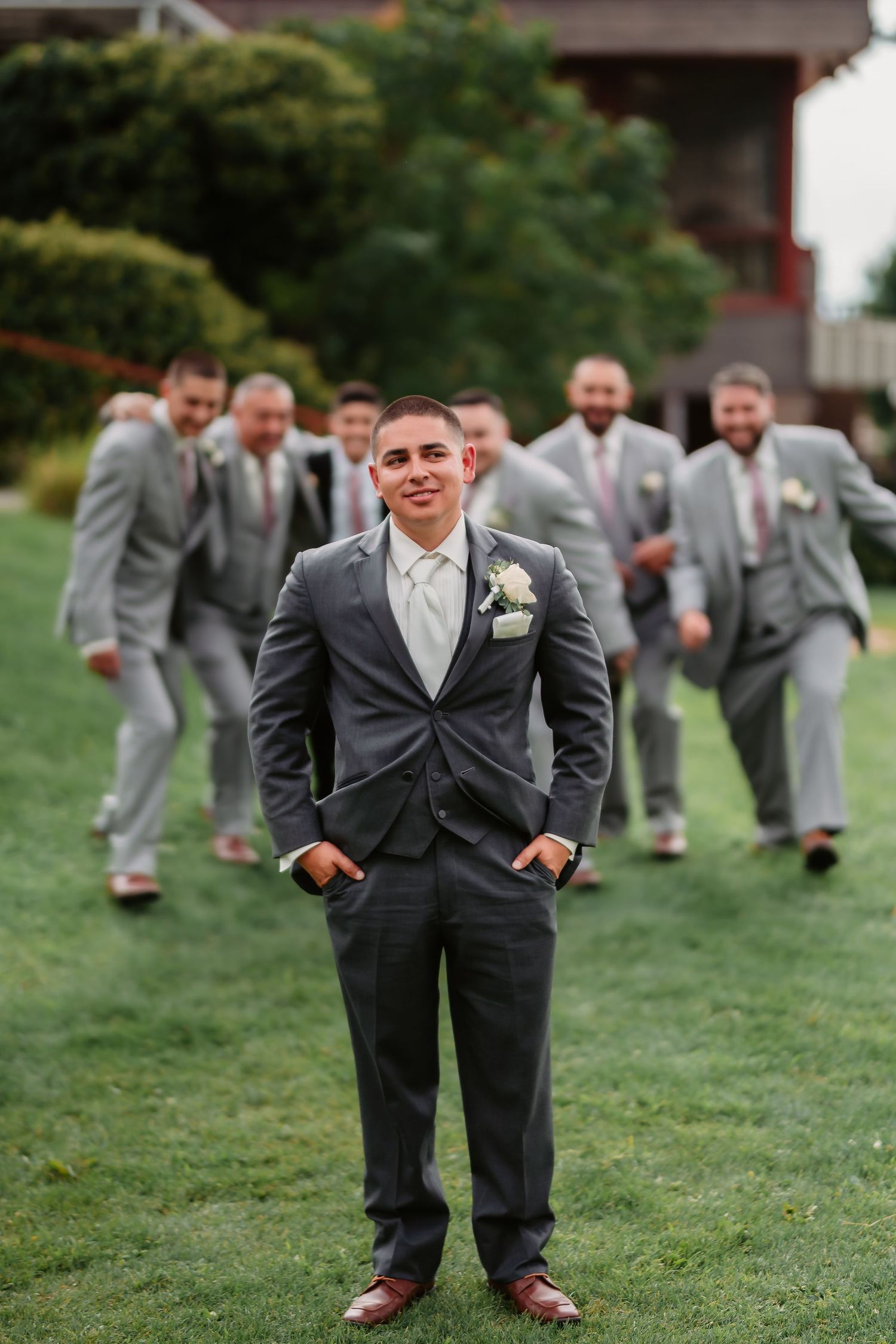 Groomsmen in gray suits having fun posing on green grass during wedding photos.