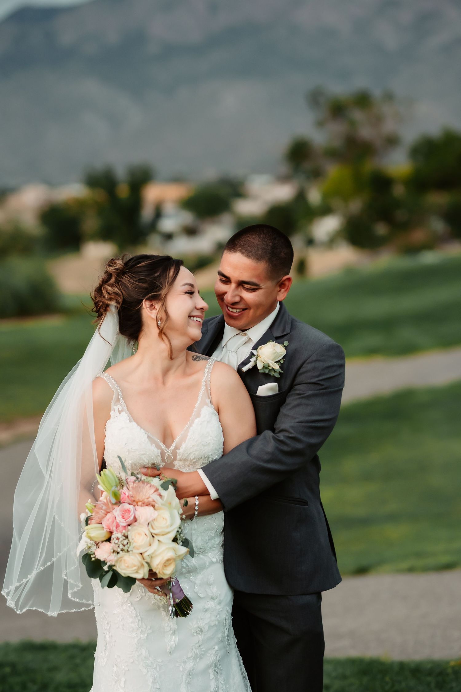 Wedding couple sharing joyful moment on grassy hillside with mountains in background.